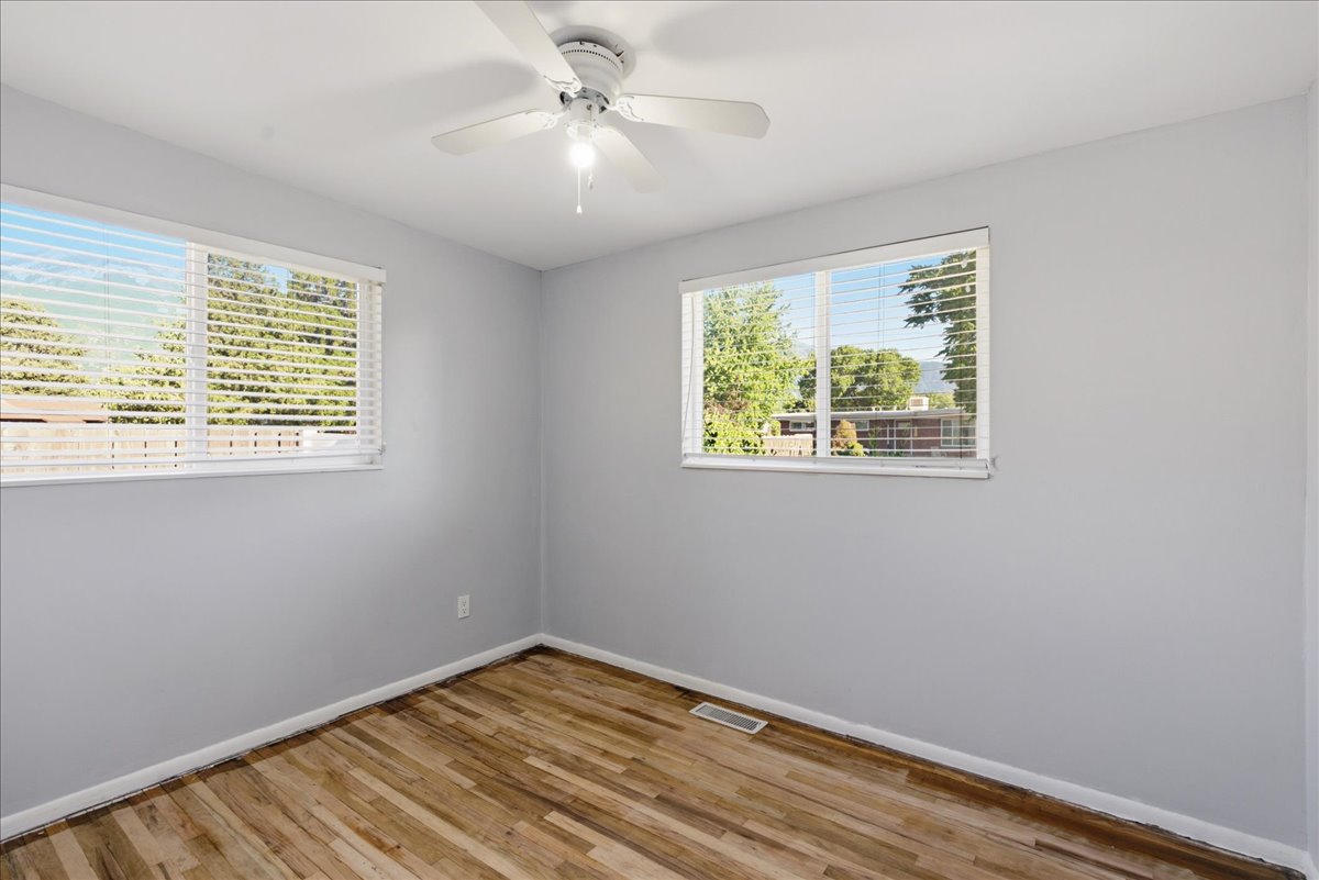 Room featuring two windows with horizontal blinds, wood-finish flooring, and light gray wall paint