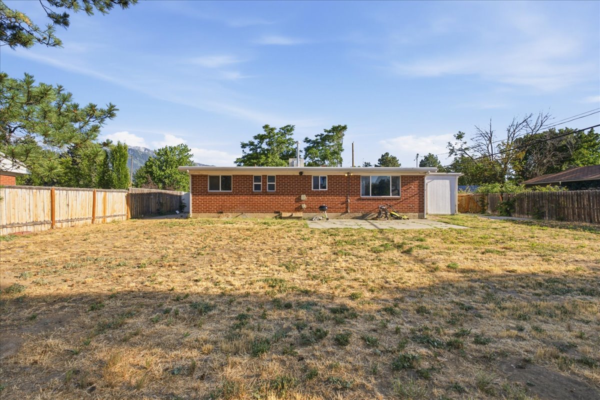 Expansive backyard featuring a brick exterior, partial wood privacy fencing, a concrete patio, and mature perimeter trees