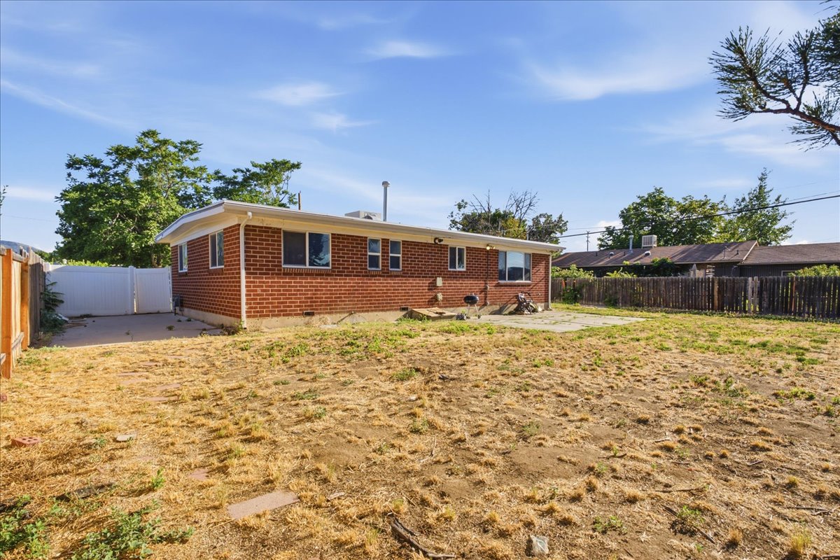 Expansive backyard featuring a red brick exterior, white trim, a concrete patio, a wooden fence, and a white privacy fence with gate