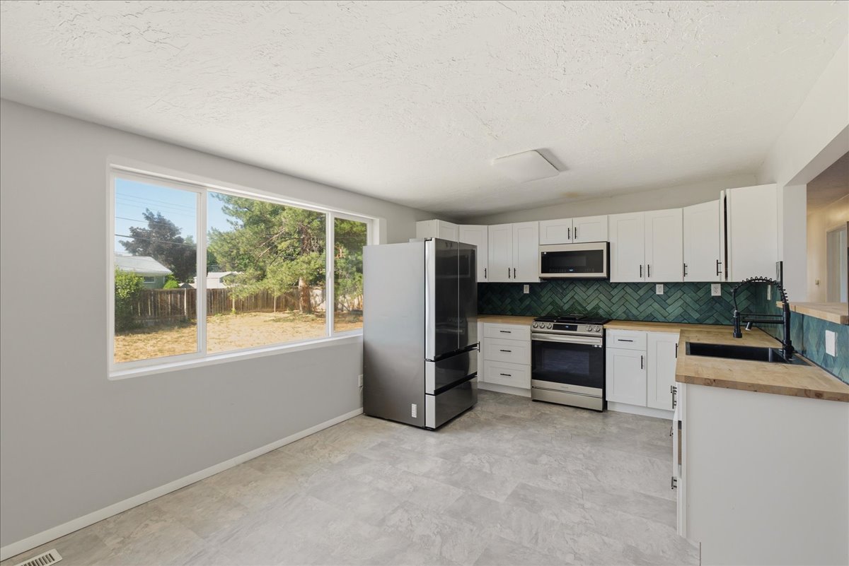 Kitchen featuring white cabinetry, light wood-finish countertops, and a green herringbone tile backsplash