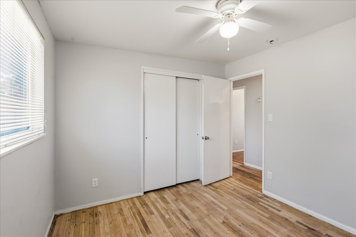 Room featuring wood-finish flooring, a window with horizontal blinds, and a ceiling fan with integrated lighting