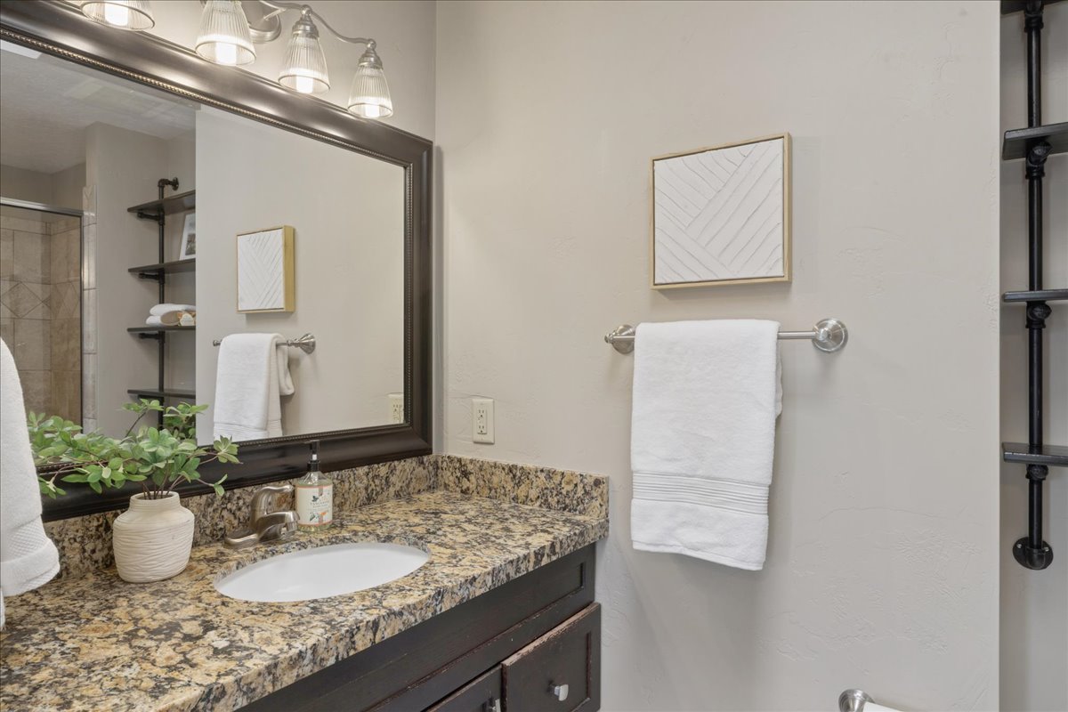 Bathroom vanity featuring a granite countertop with an undermount sink, dark wood cabinetry, and a large framed mirror with a four-light fixture