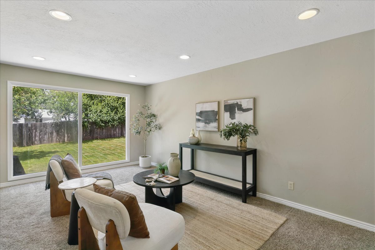 Spacious living area featuring a large window overlooking a private backyard with mature trees, recessed lighting, and light-toned wall paint