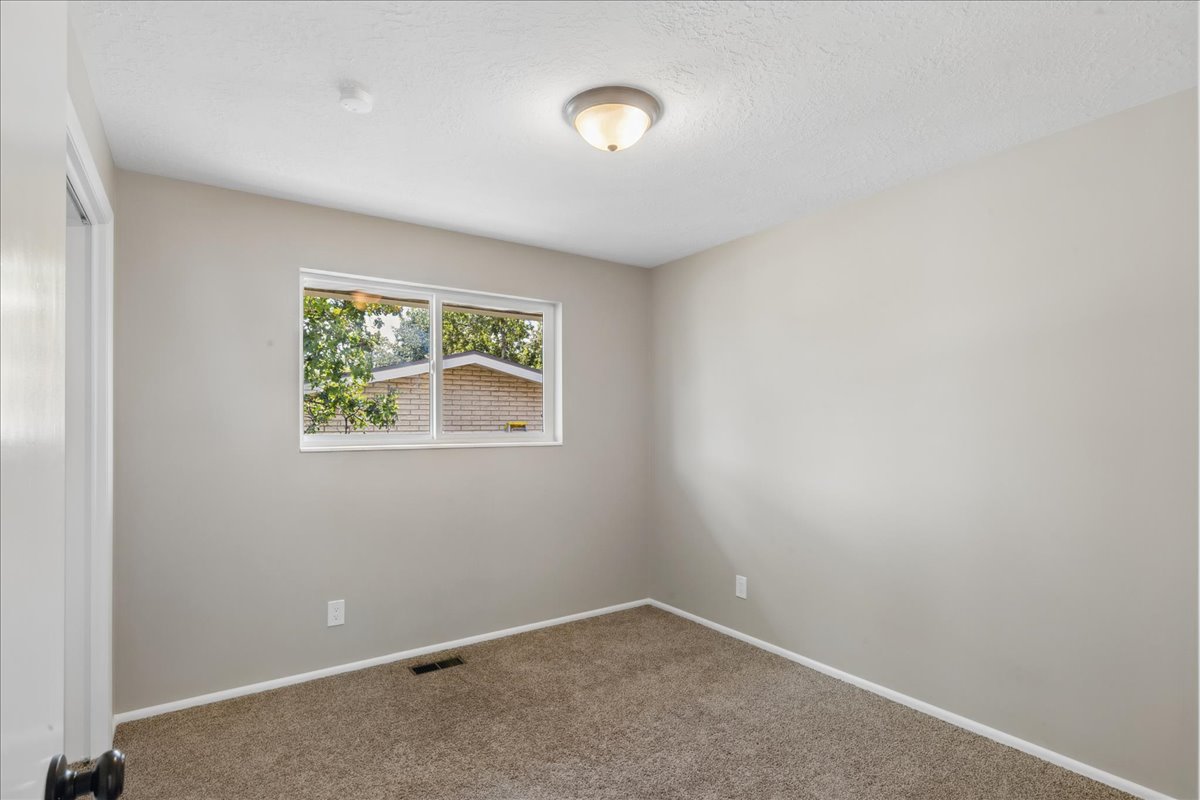 Neutral-toned bedroom featuring a double-pane window, flush-mount ceiling light, and carpet flooring