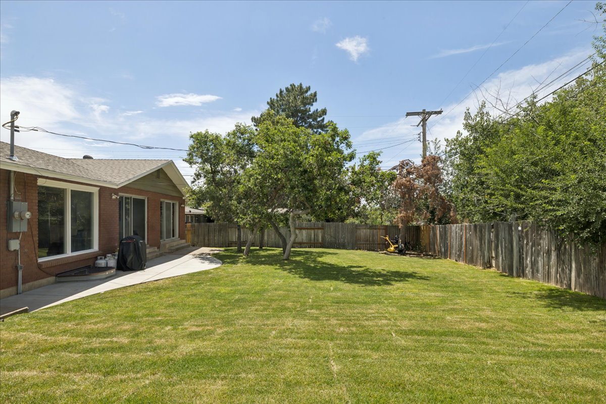 Spacious backyard featuring a manicured lawn, established trees, a privacy fence, and a concrete patio