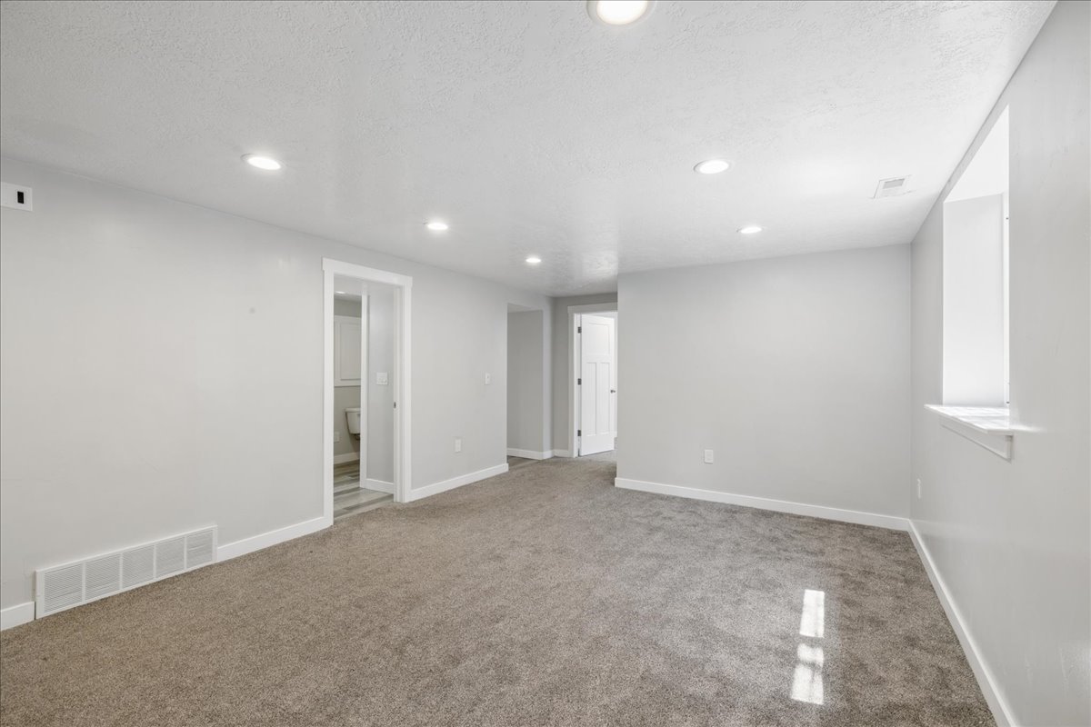 Spacious room featuring gray carpet, light gray walls, recessed lighting, and a white-trimmed window