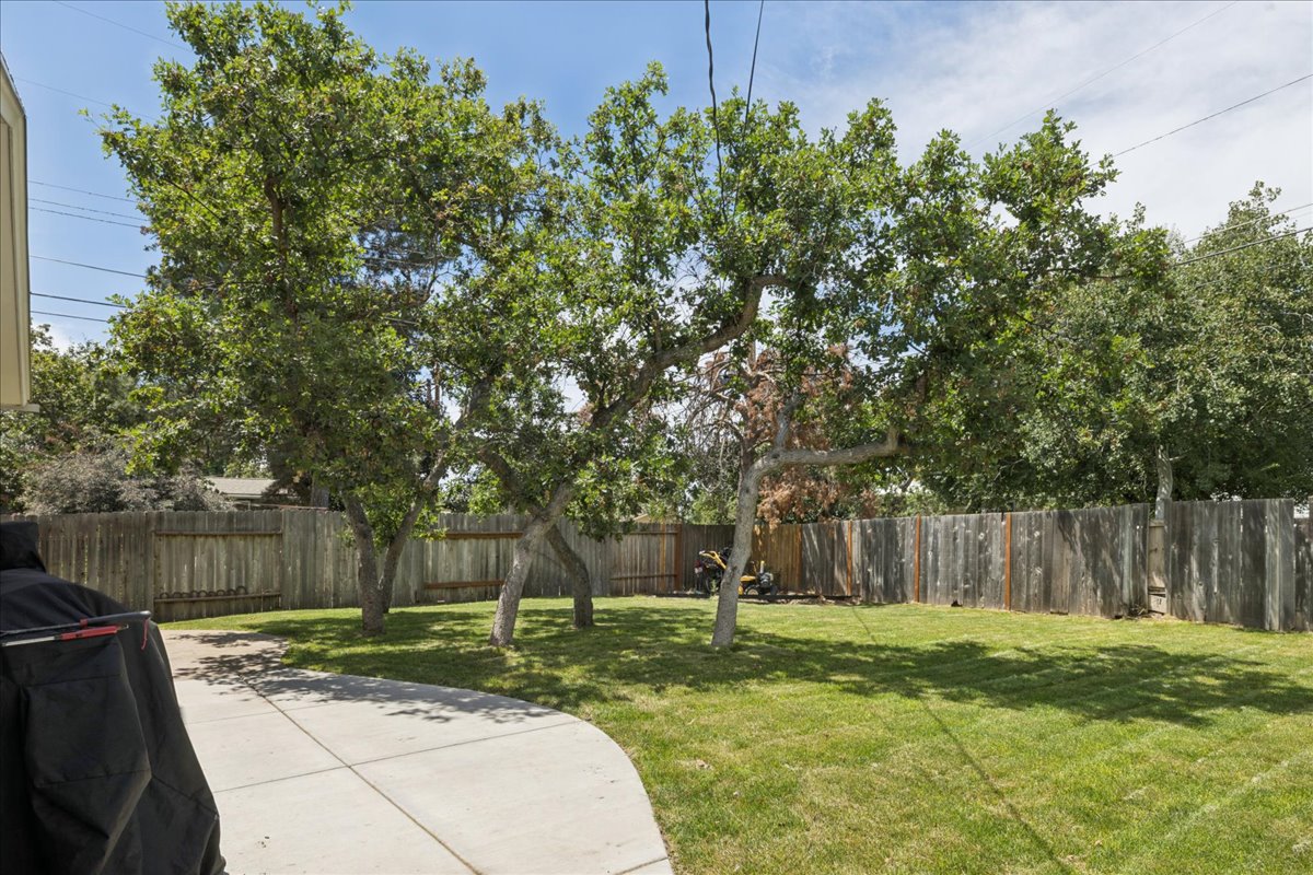 Spacious backyard featuring a manicured lawn, mature trees, a concrete patio, and a wood privacy fence