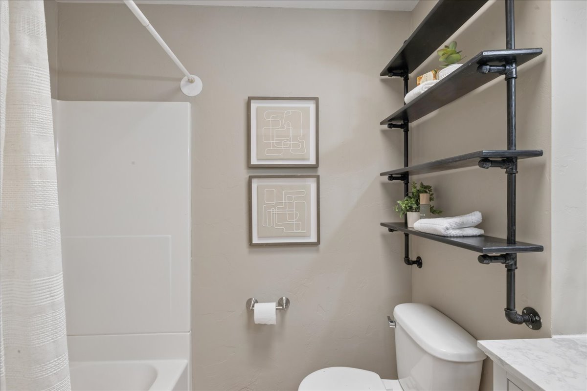 Bathroom featuring a white tub/shower combination, industrial-style pipe shelving, and neutral wall paint