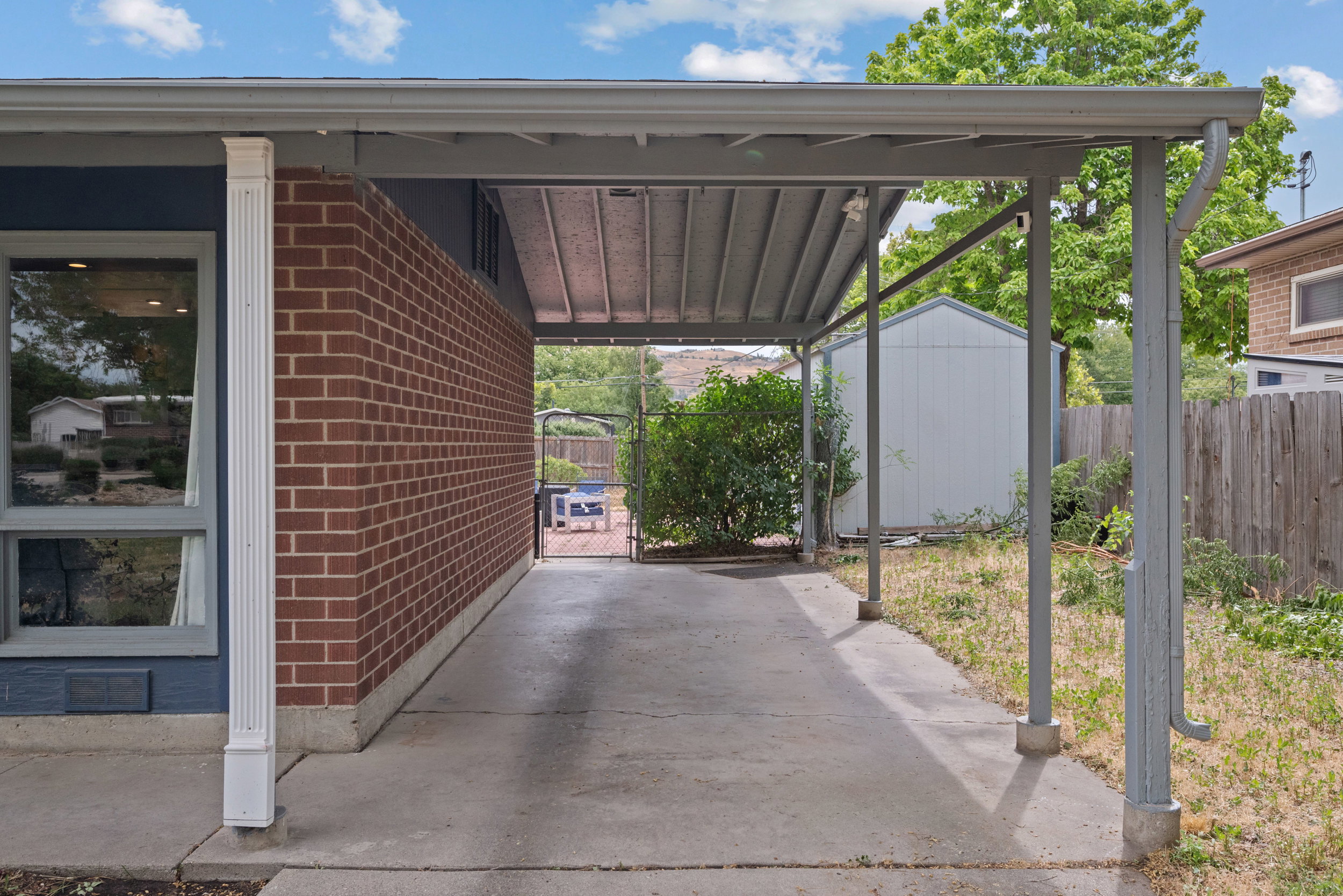 Covered carport area featuring a concrete drive, brick exterior wall, and a side window