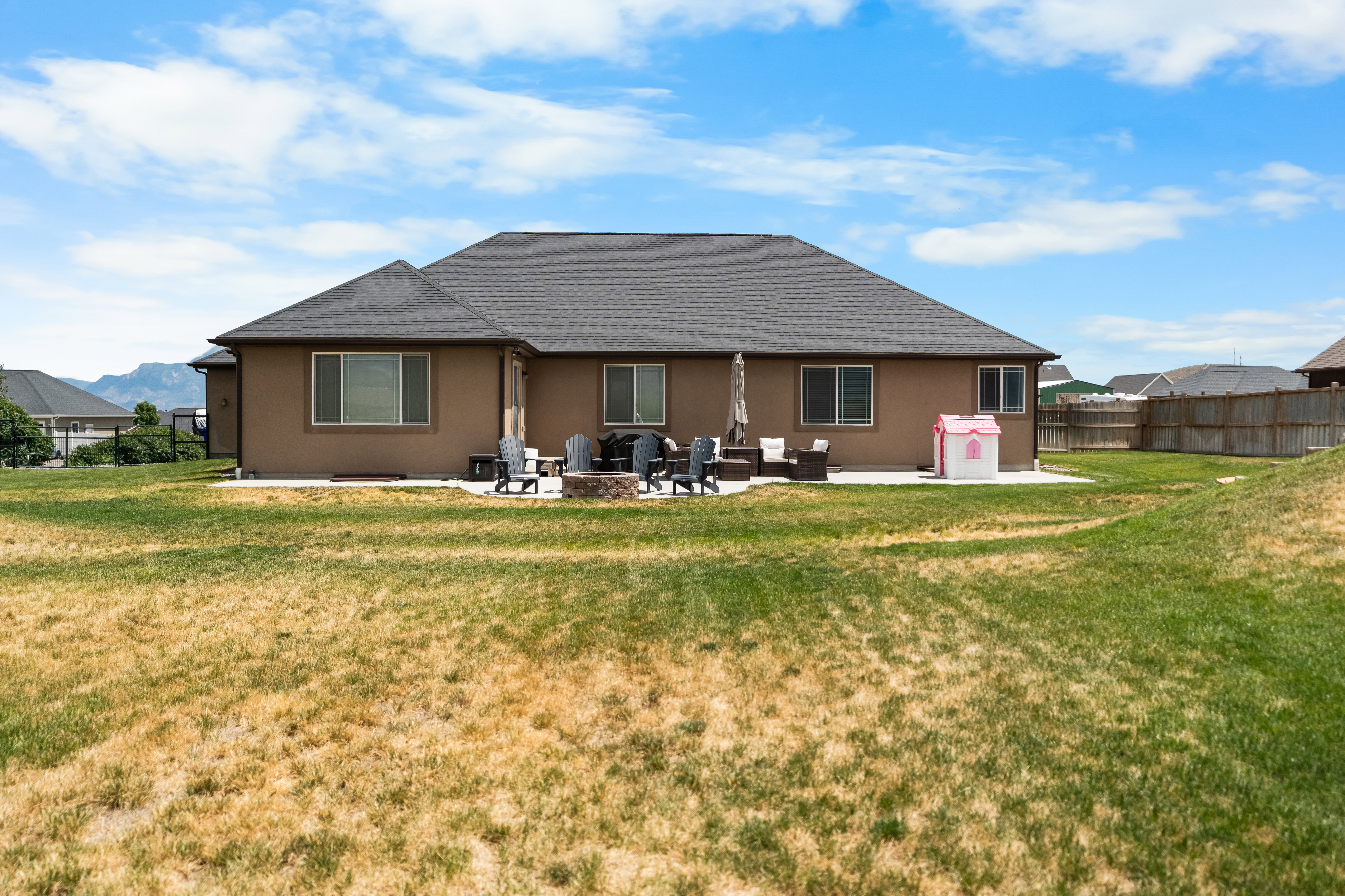 Rear exterior featuring a spacious patio, built-in fire pit, multiple windows, and a dark shingle roof