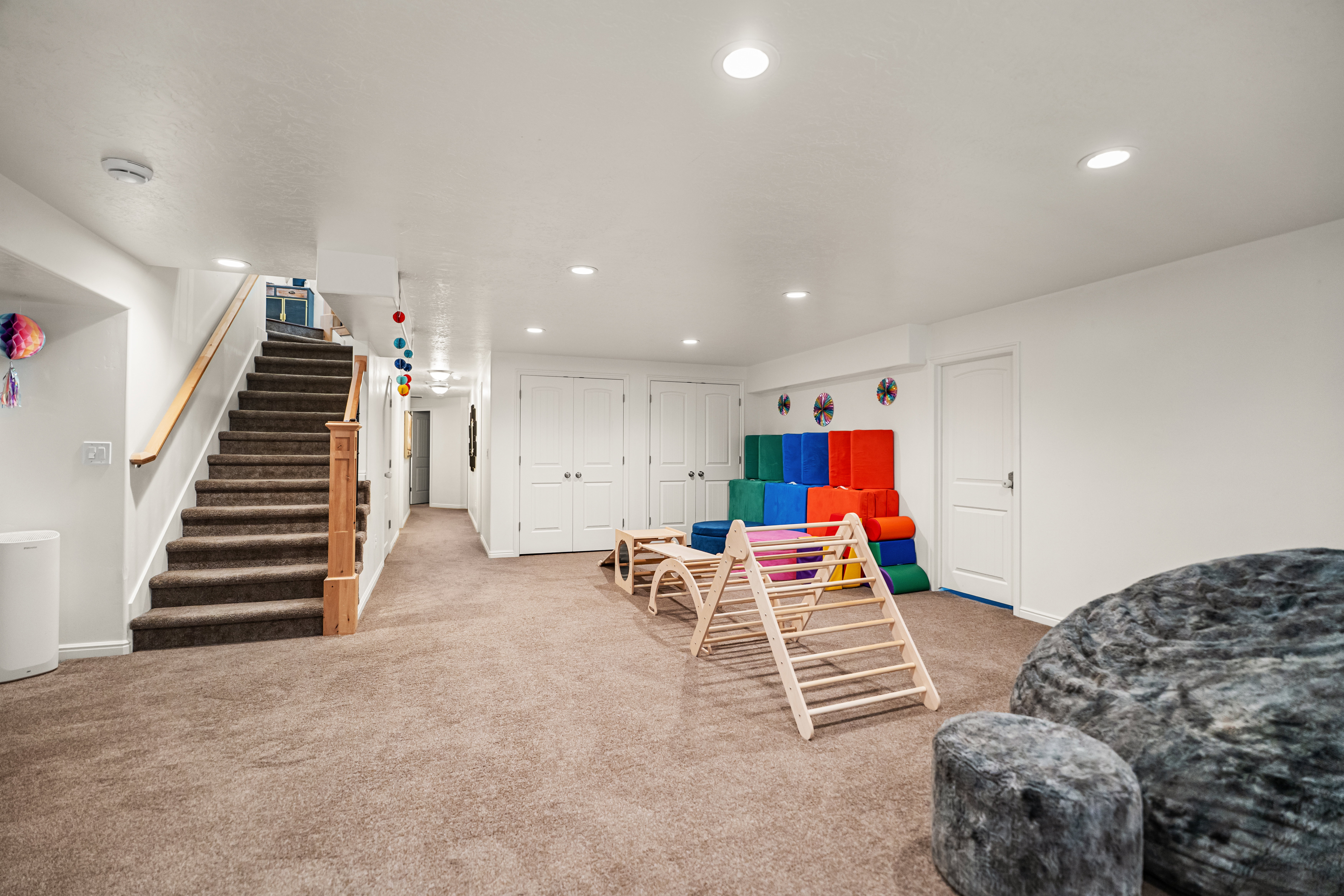 Spacious lower-level room featuring plush carpeting, recessed lighting, white painted walls, and a carpeted staircase with a wood handrail and newel post