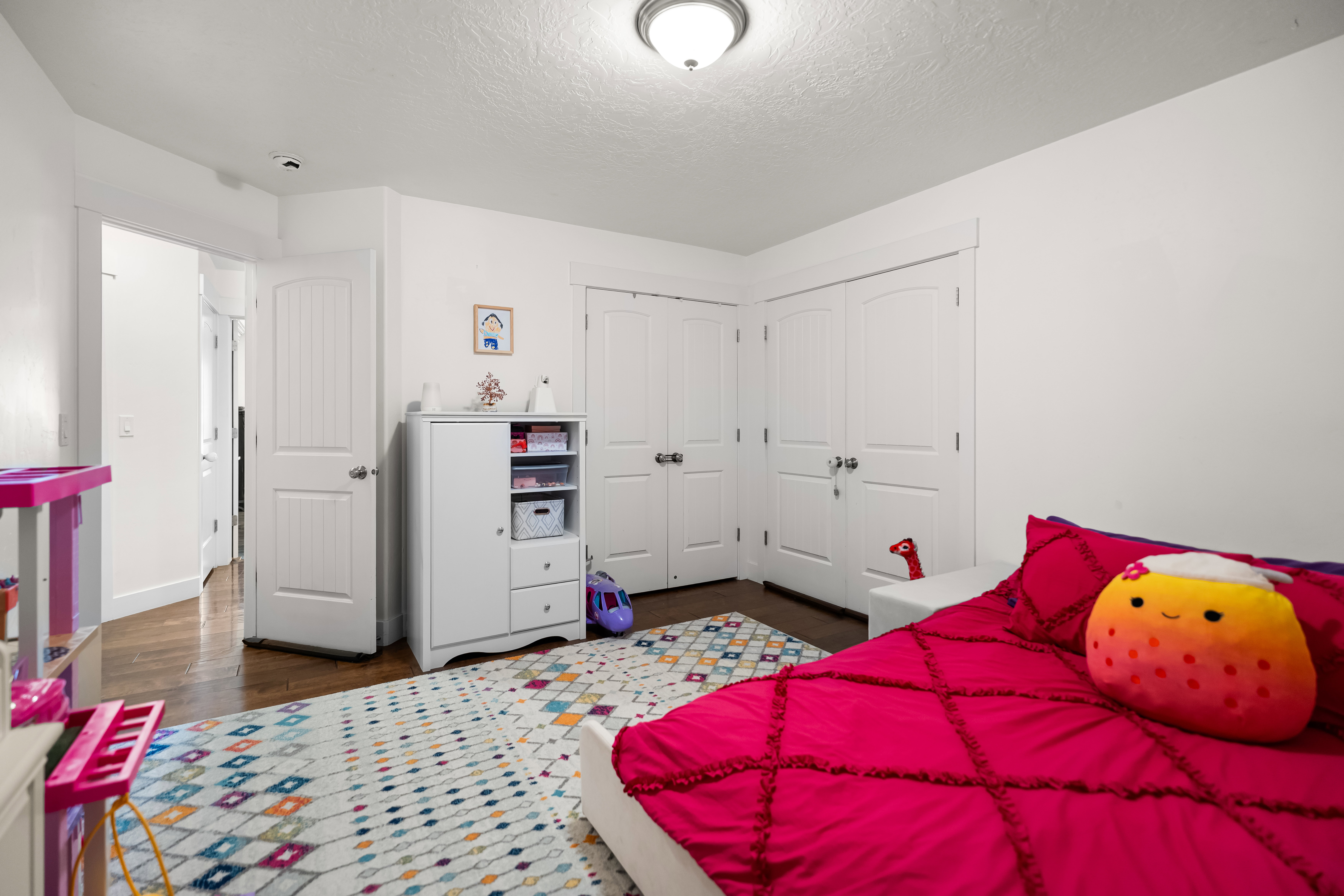 Bright bedroom featuring wood-finish flooring, white walls, and multiple white paneled doors