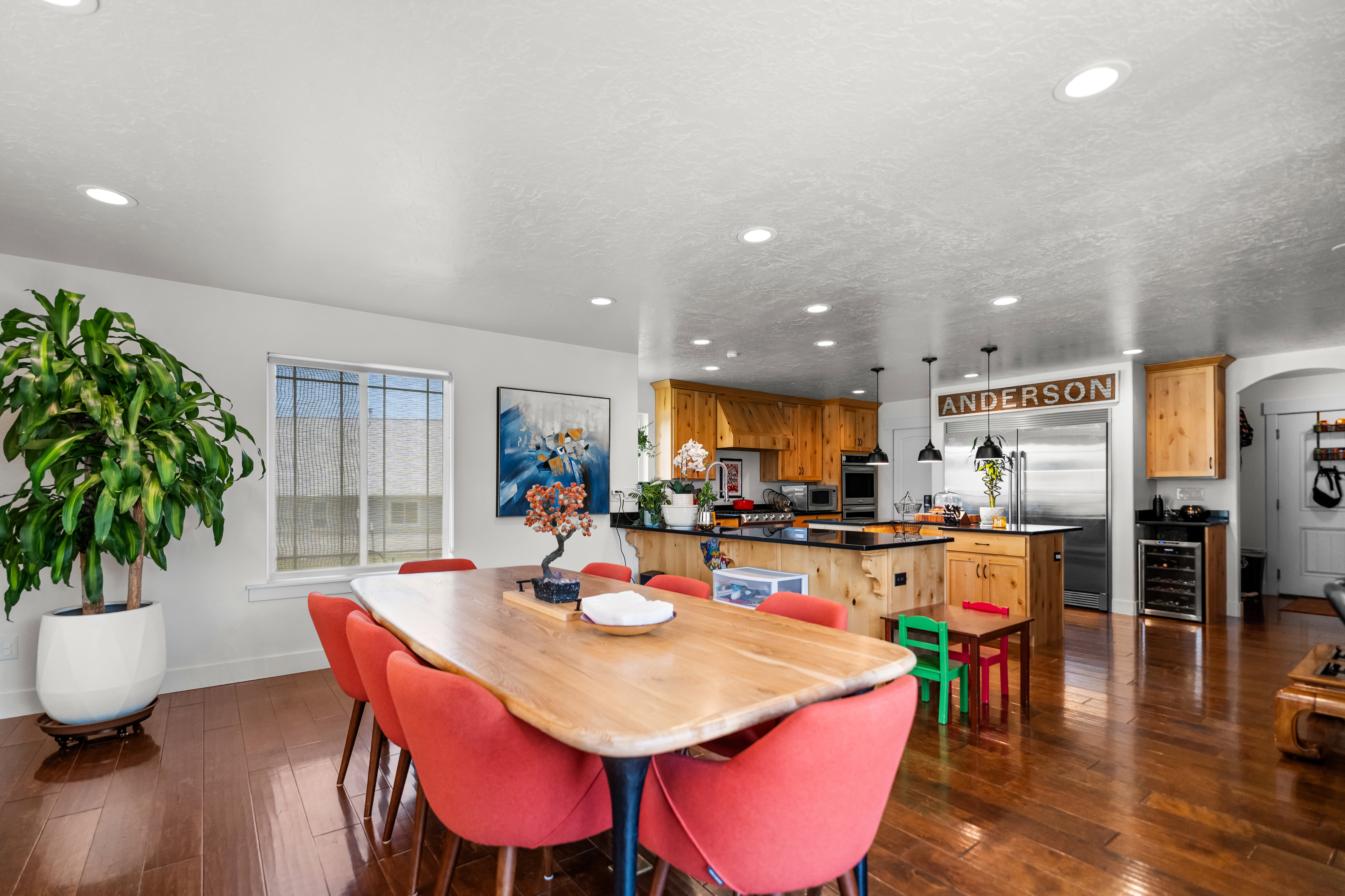Open-concept living area featuring rich wood-finish flooring, recessed lighting, a built-in wine refrigerator, and a kitchen island with dark countertops