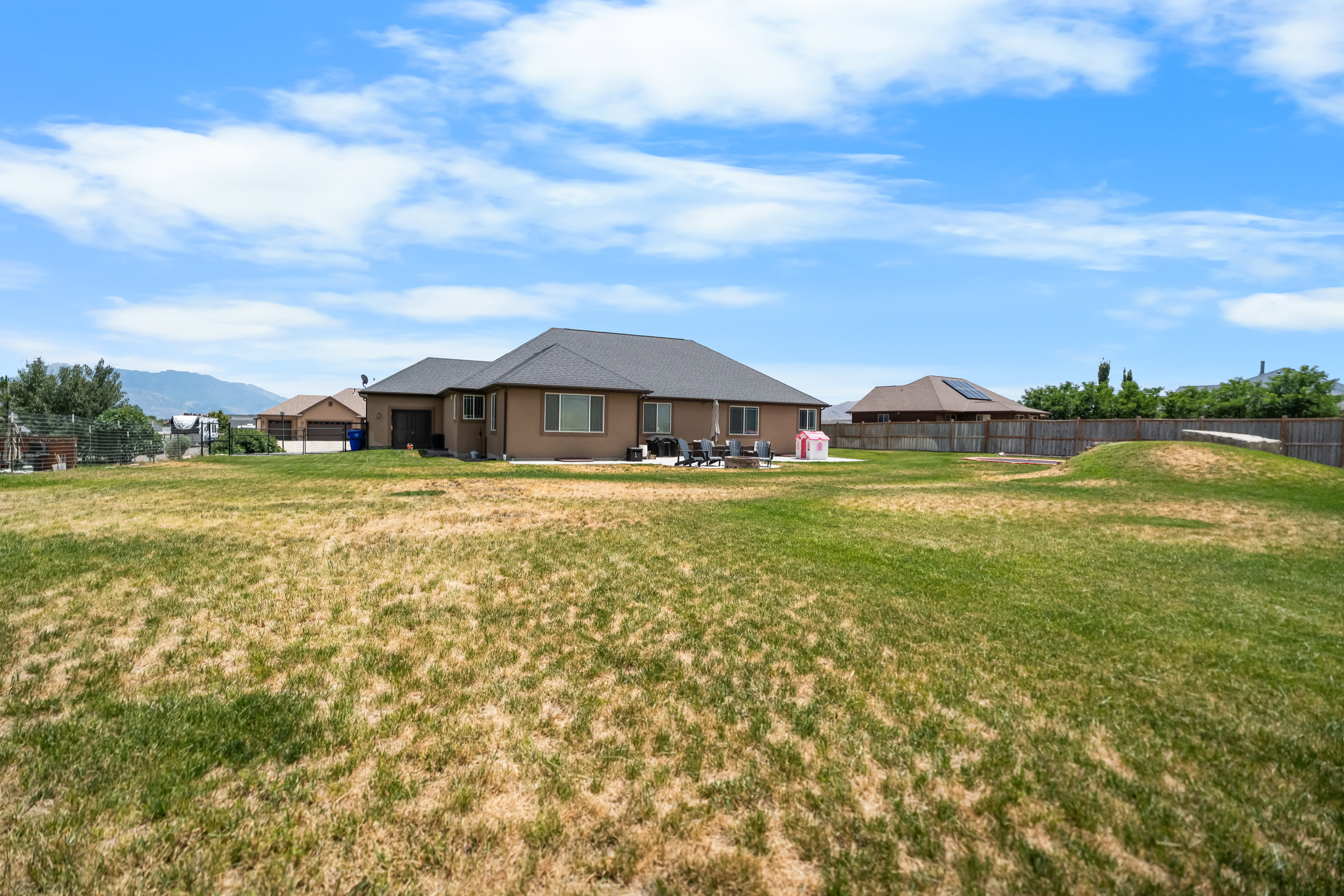 Expansive backyard featuring a patio area, mature fencing, and distant mountain scenery