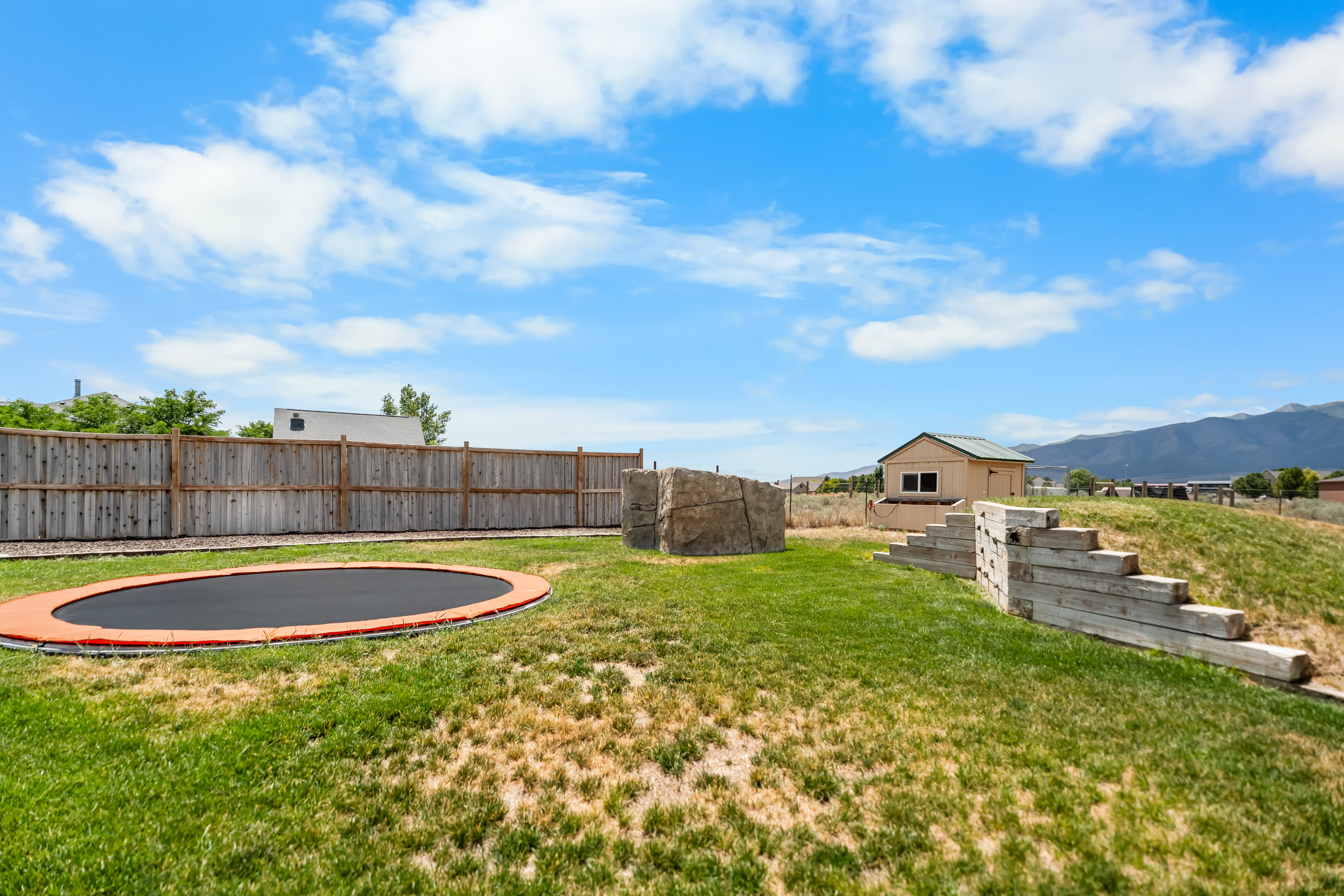 Expansive backyard featuring a built-in trampoline, wood privacy fencing, tiered retaining wall, and a detached shed