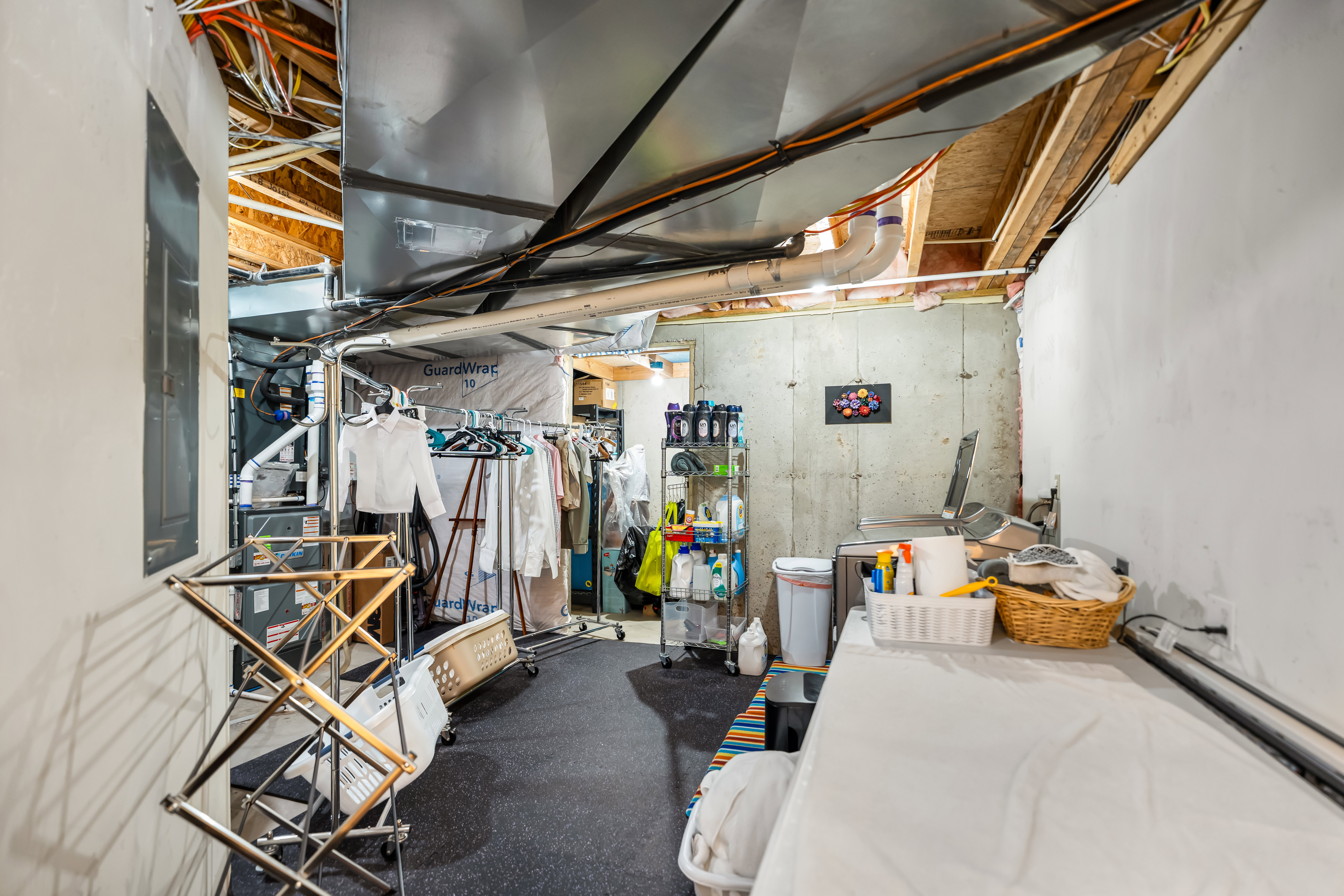 Unfinished basement area featuring exposed ceiling joists and ductwork, a utility sink, and concrete walls
