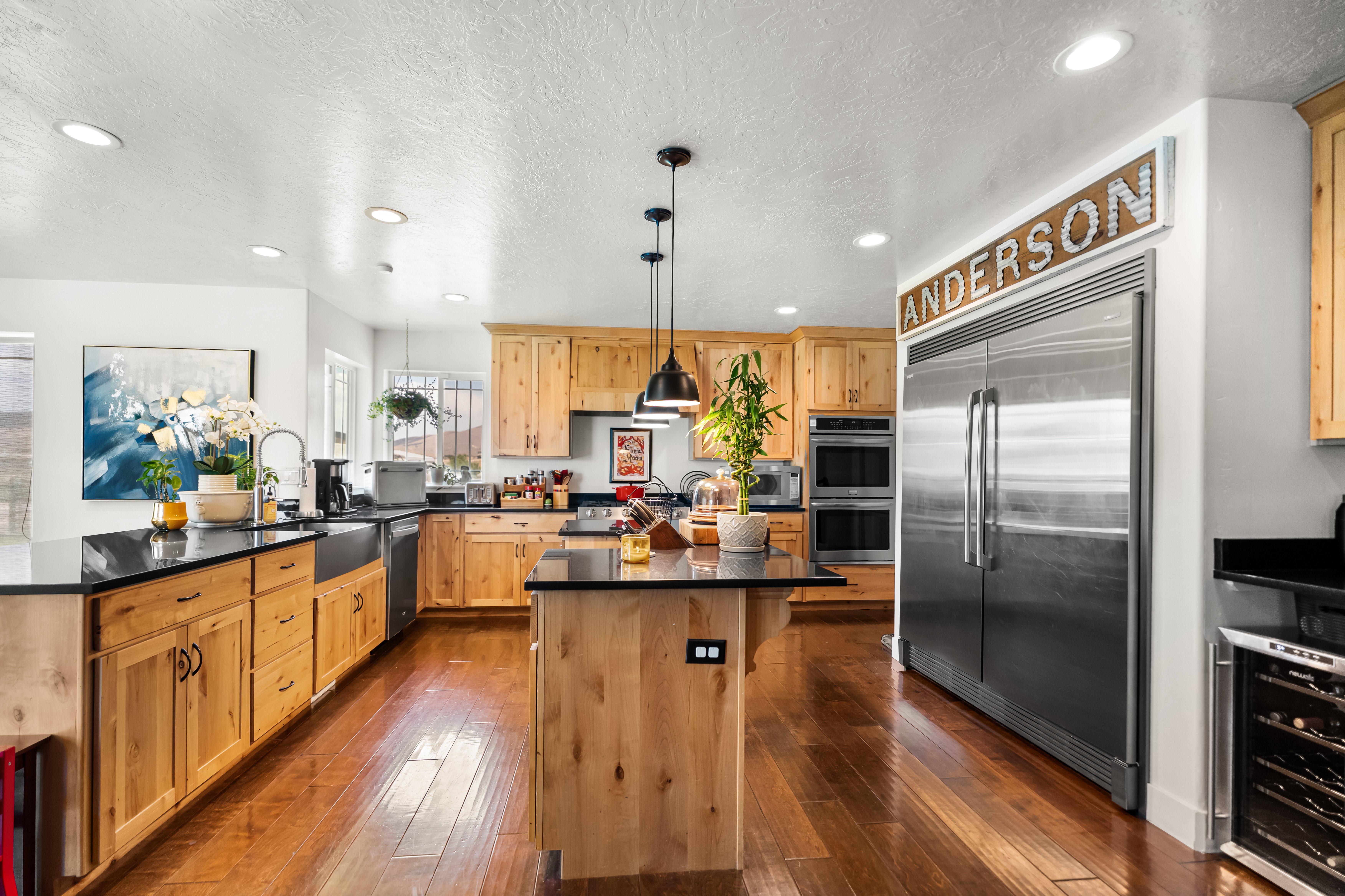 Kitchen featuring wood-finish flooring, natural wood cabinetry, black countertops, and stainless steel appliances