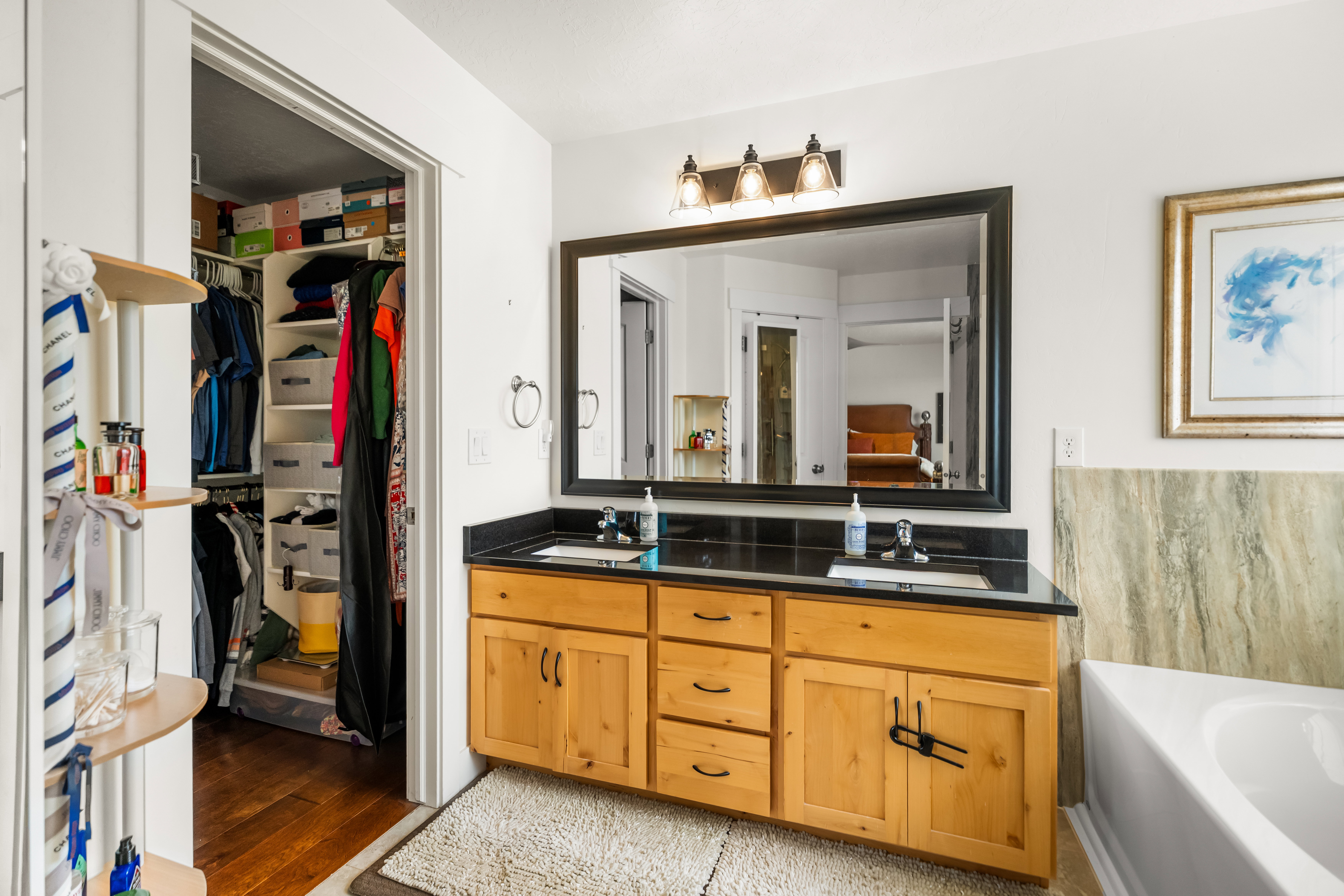 Double vanity with black countertop and light wood cabinetry, featuring a large mirror and three-light fixture