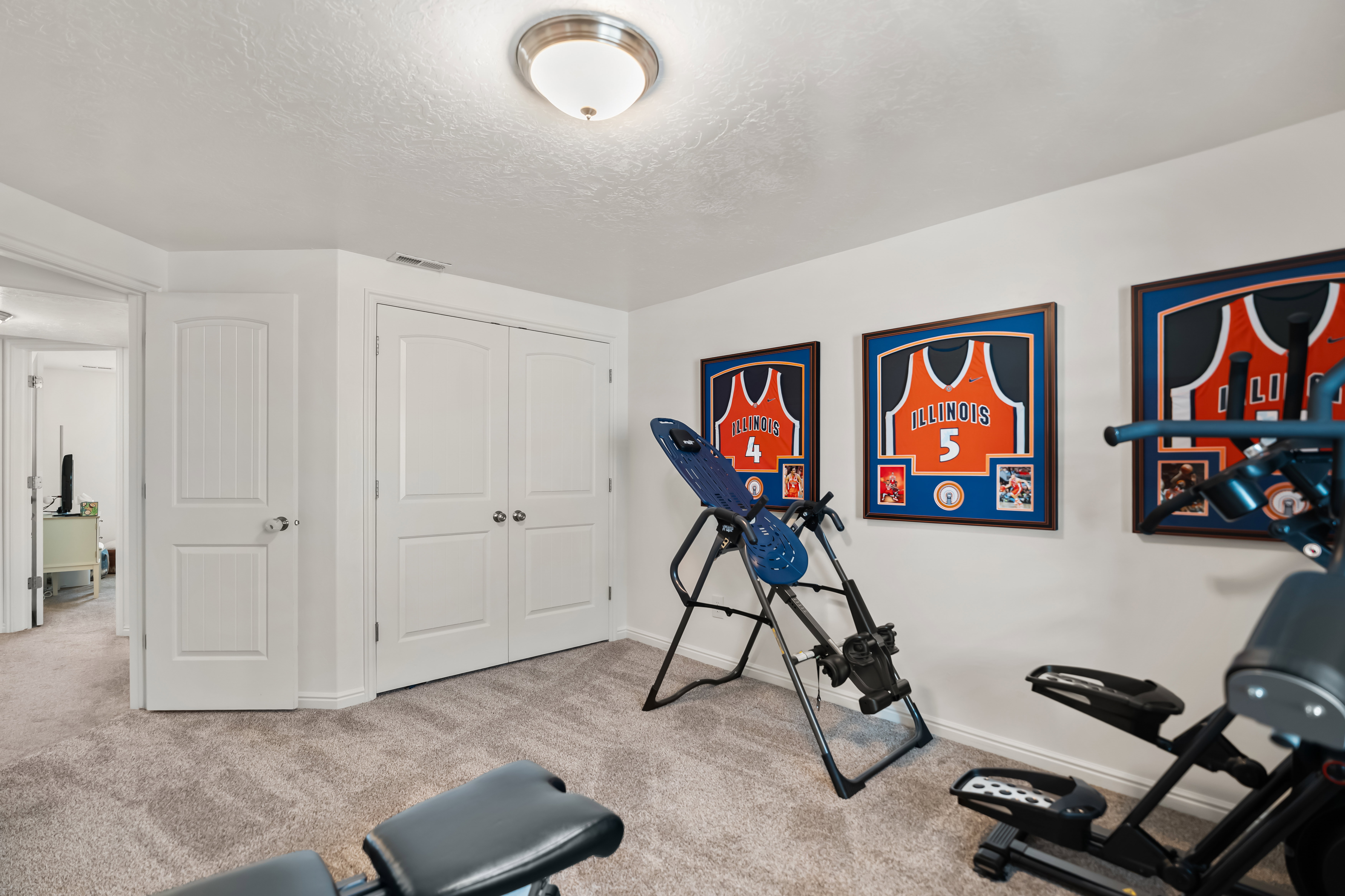 Carpeted room featuring white walls, a flush-mount ceiling light fixture, and white bi-fold closet doors with round hardware