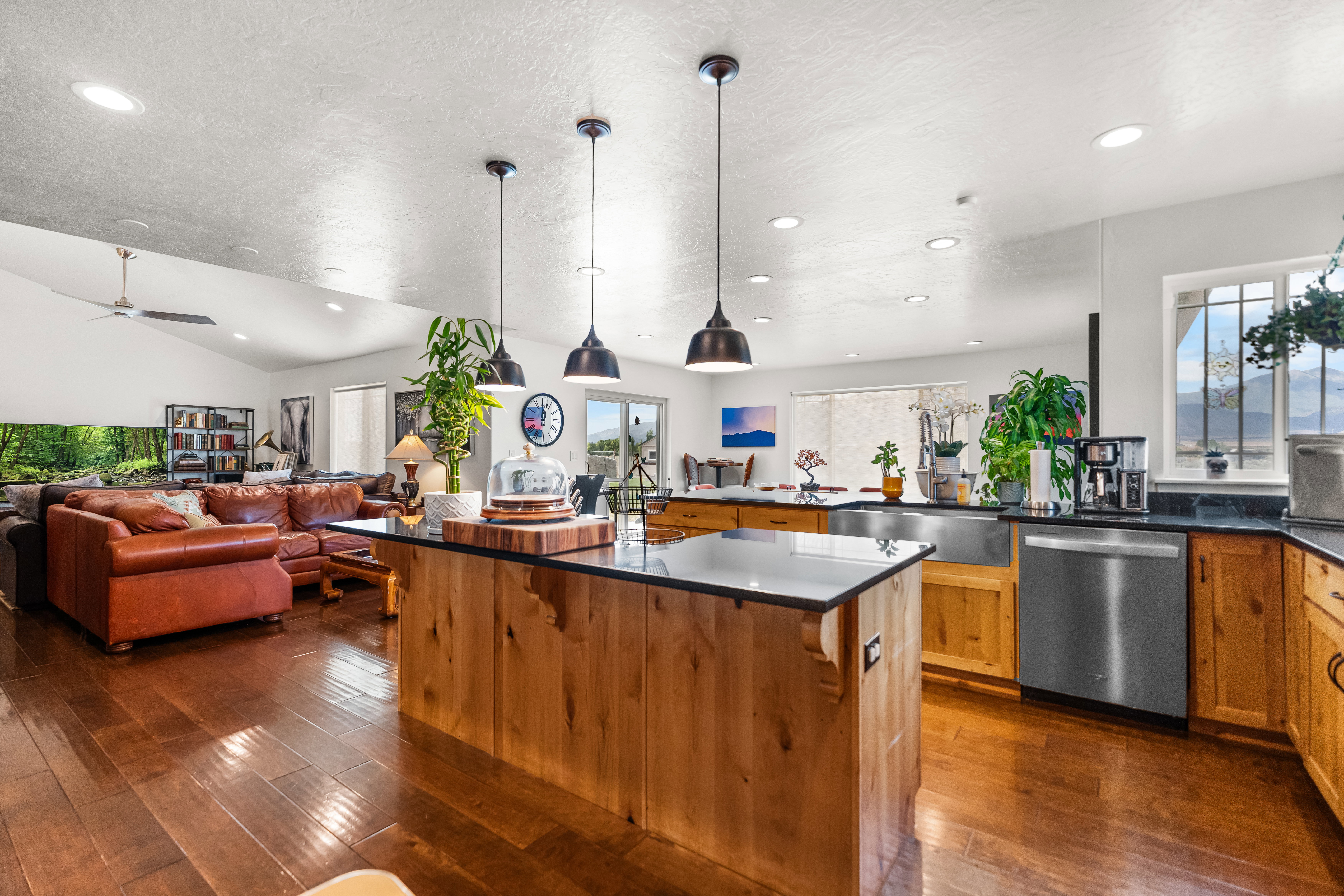 Open-concept living space featuring wood-finish flooring, a kitchen island with pendant lighting and a dark countertop, and wood cabinetry with stainless steel appliances