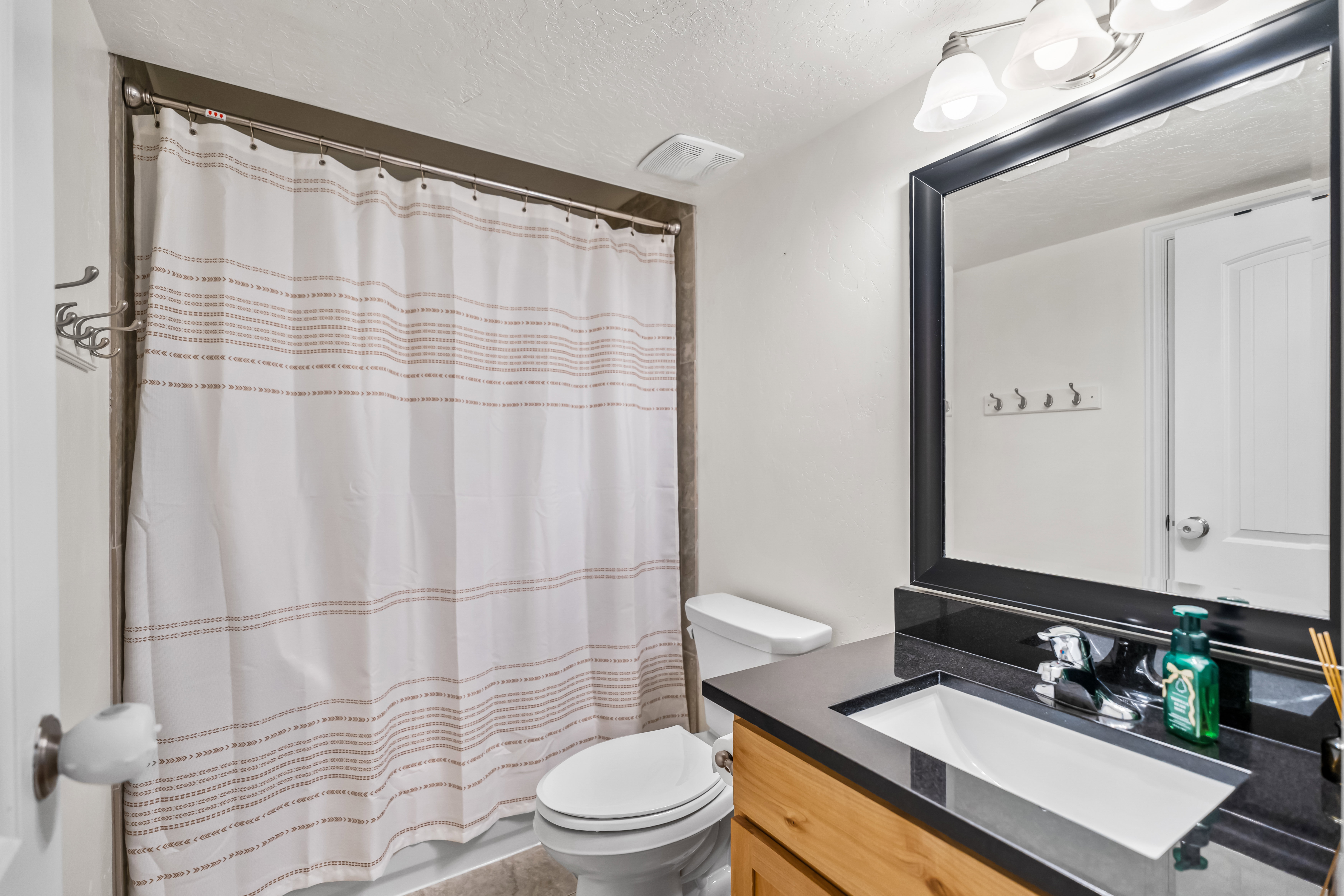 Bathroom featuring a dark framed mirror, vanity lighting, a wood-finish vanity with an integrated sink, dark countertop, and a shower/tub combination