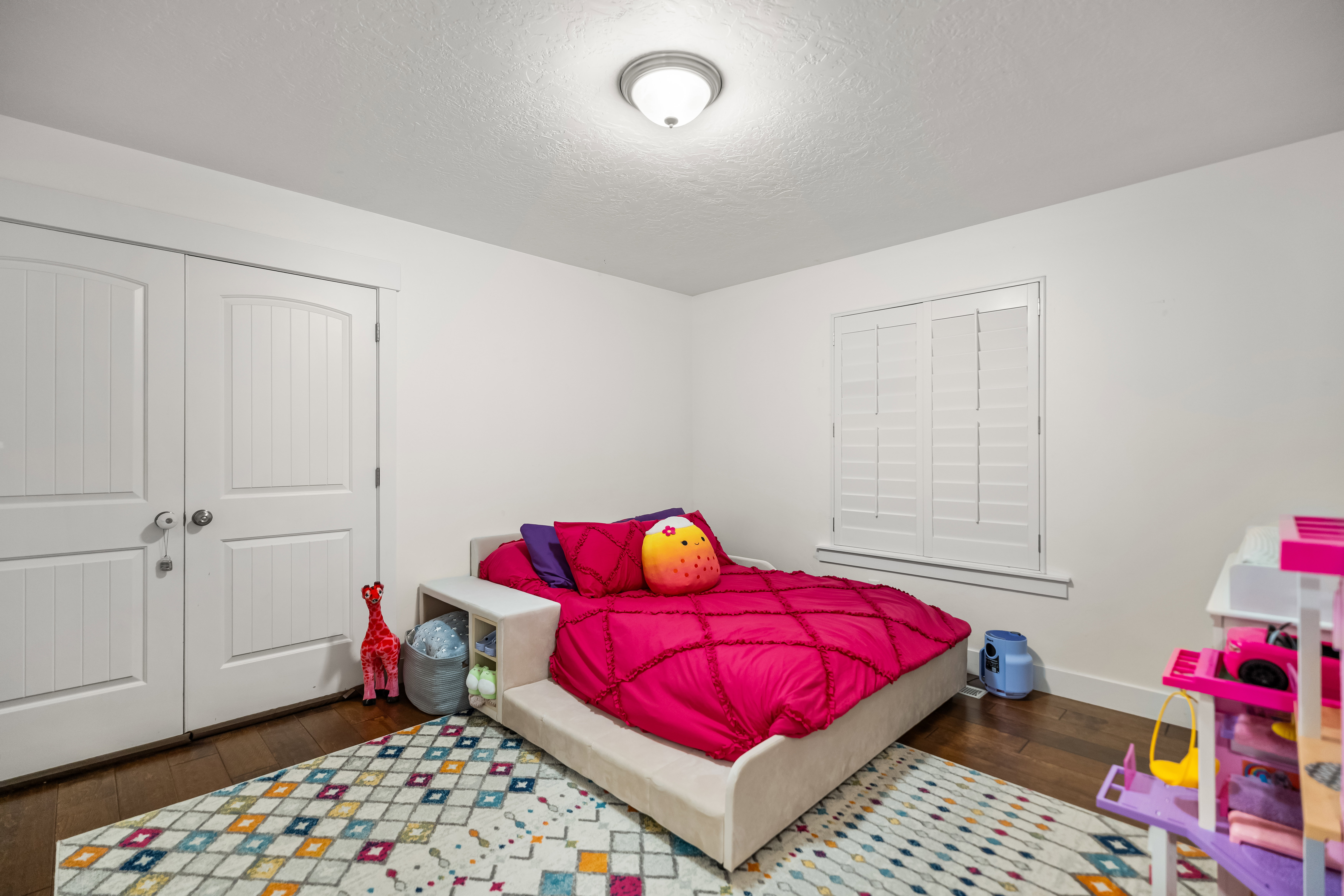 Bedroom featuring dark wood-finish flooring, white walls, and a window with white plantation shutters