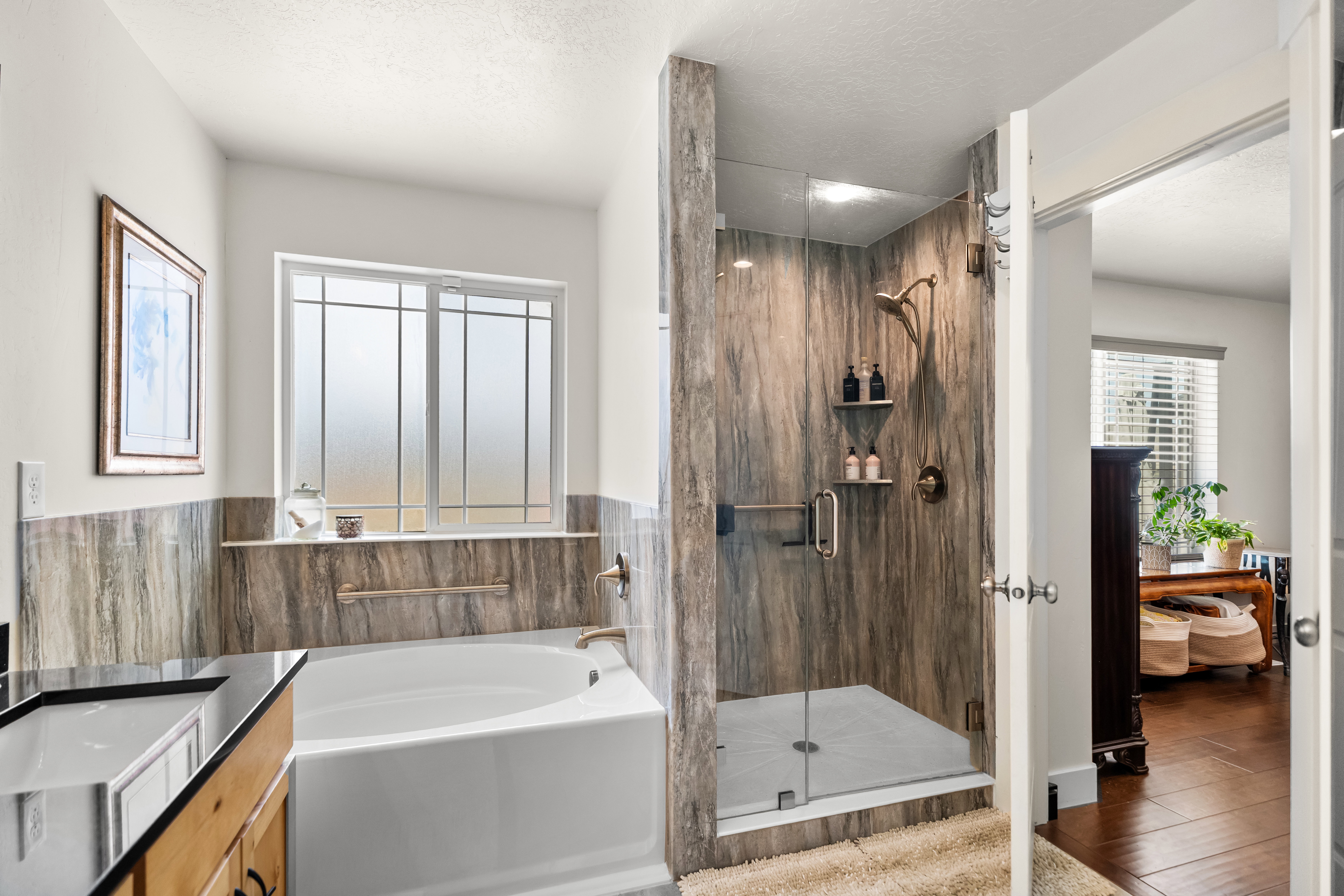 Bathroom featuring a built-in soaking tub, a large glass-enclosed shower with paneling, a vanity with a dark countertop, and a window with frosted panes