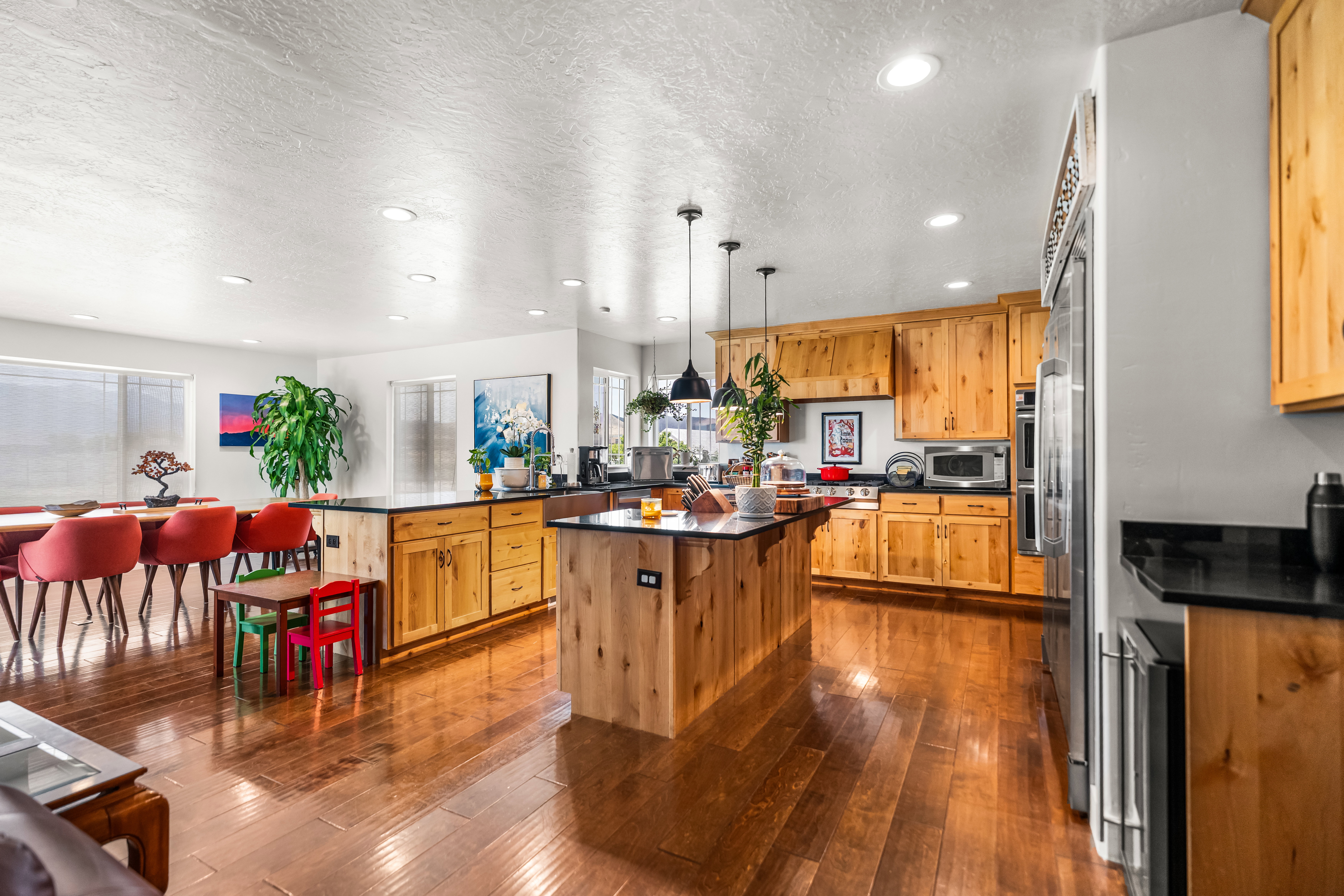 Open-concept kitchen and dining area featuring wood-finish flooring, natural wood cabinetry, dark countertops, and stainless steel appliances