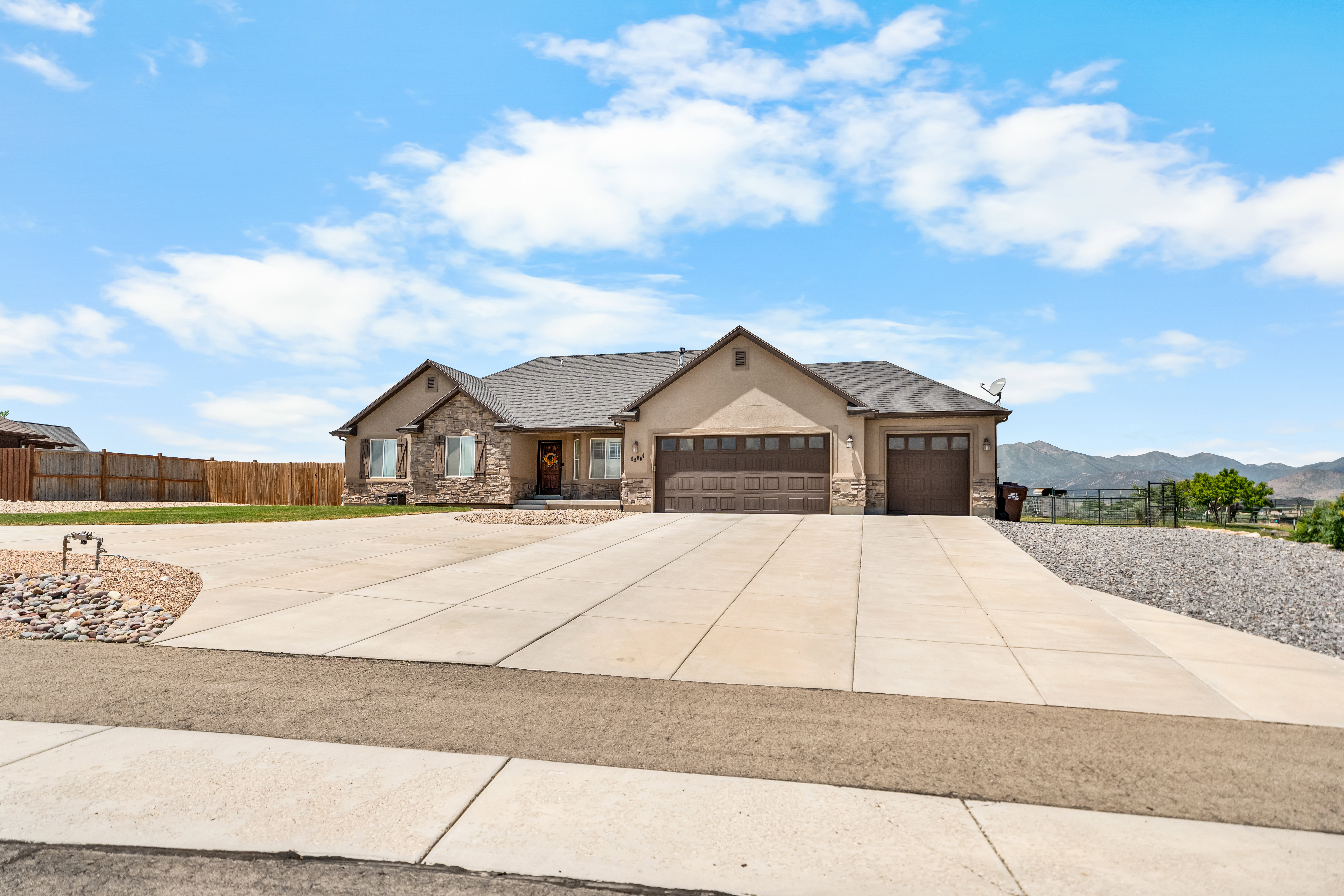 Ranch-style residence featuring a stucco and stone facade, dark roof, and a large concrete driveway