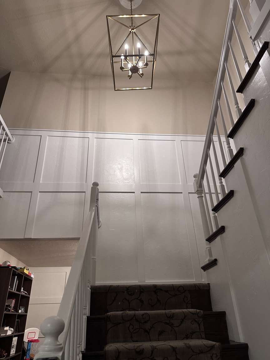 Two-story entryway featuring wainscoting, an ornate chandelier, and a carpeted staircase with white balusters