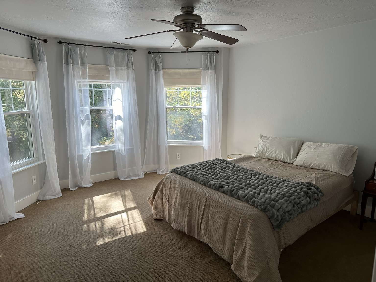 Bedroom featuring a ceiling fan with integrated lighting, multiple windows, and neutral carpeting