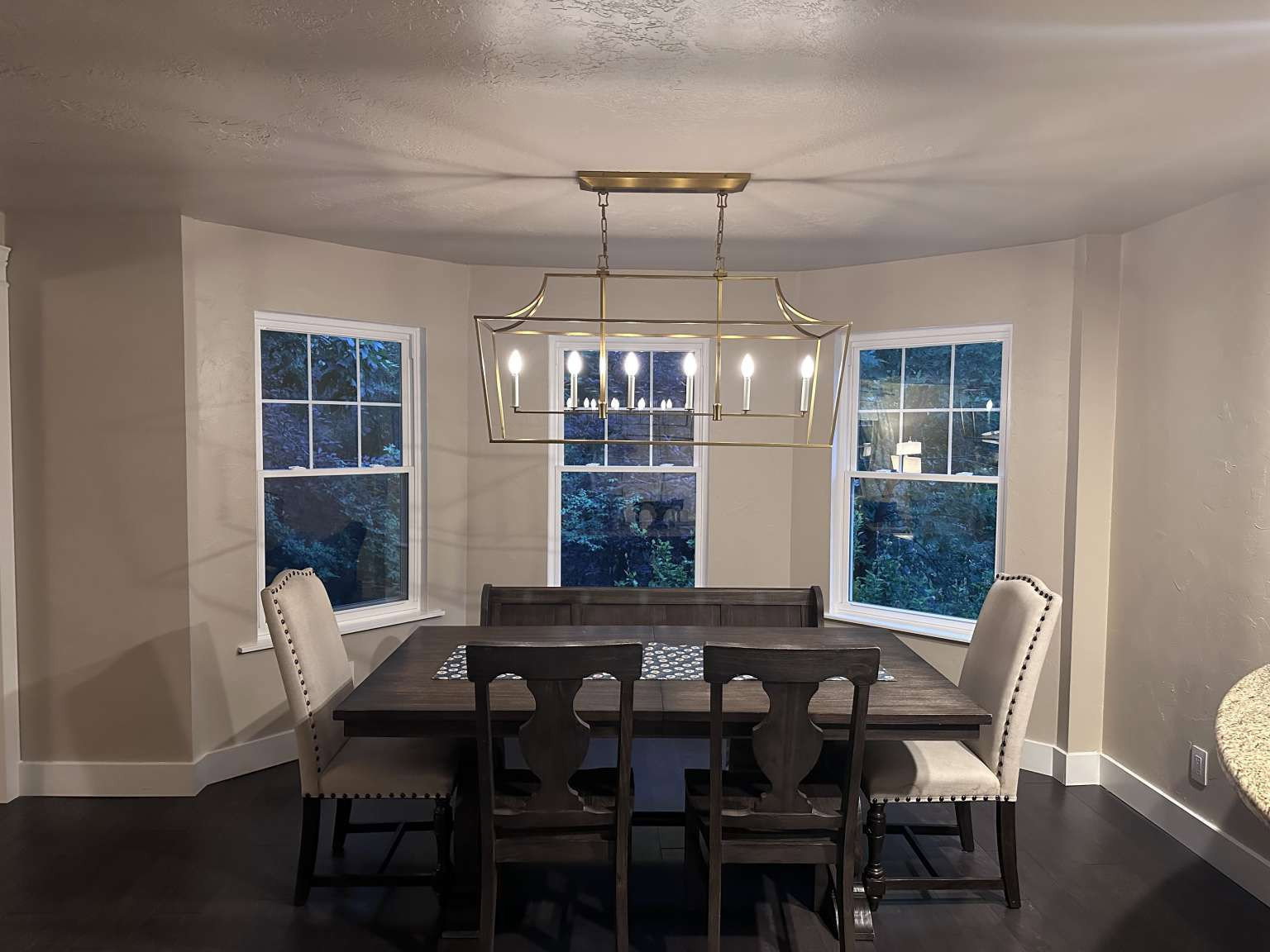 Dining area featuring dark wood-finish flooring, light tan walls, and a bay window configuration with three double-hung windows