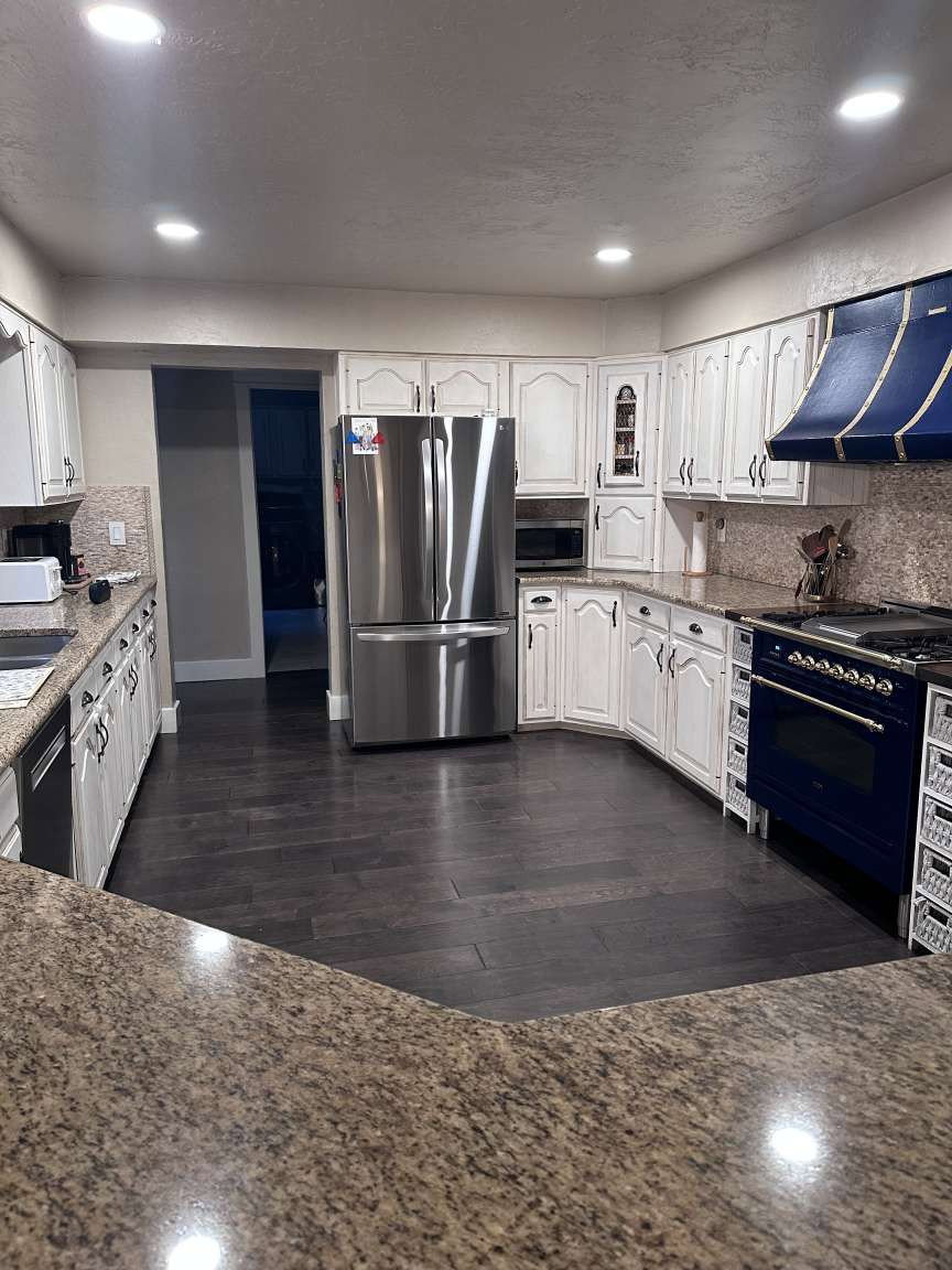 Kitchen featuring granite-style countertops, dark wood-finish flooring, white cabinetry with decorative trim, a stainless steel refrigerator, and a blue range with a matching custom hood