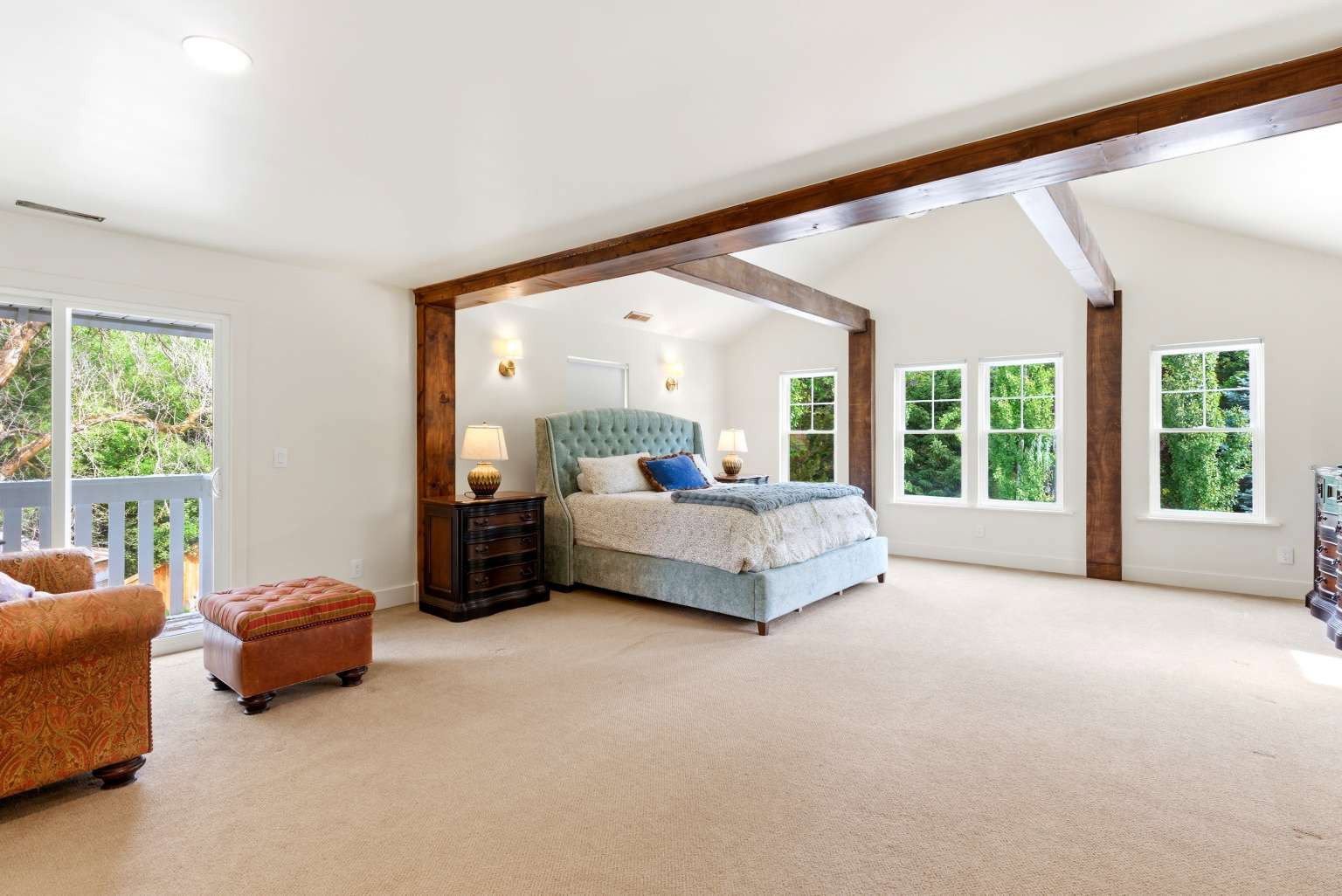Spacious room featuring vaulted ceilings with exposed wood beams, light-toned carpeting, and a private balcony with white railings