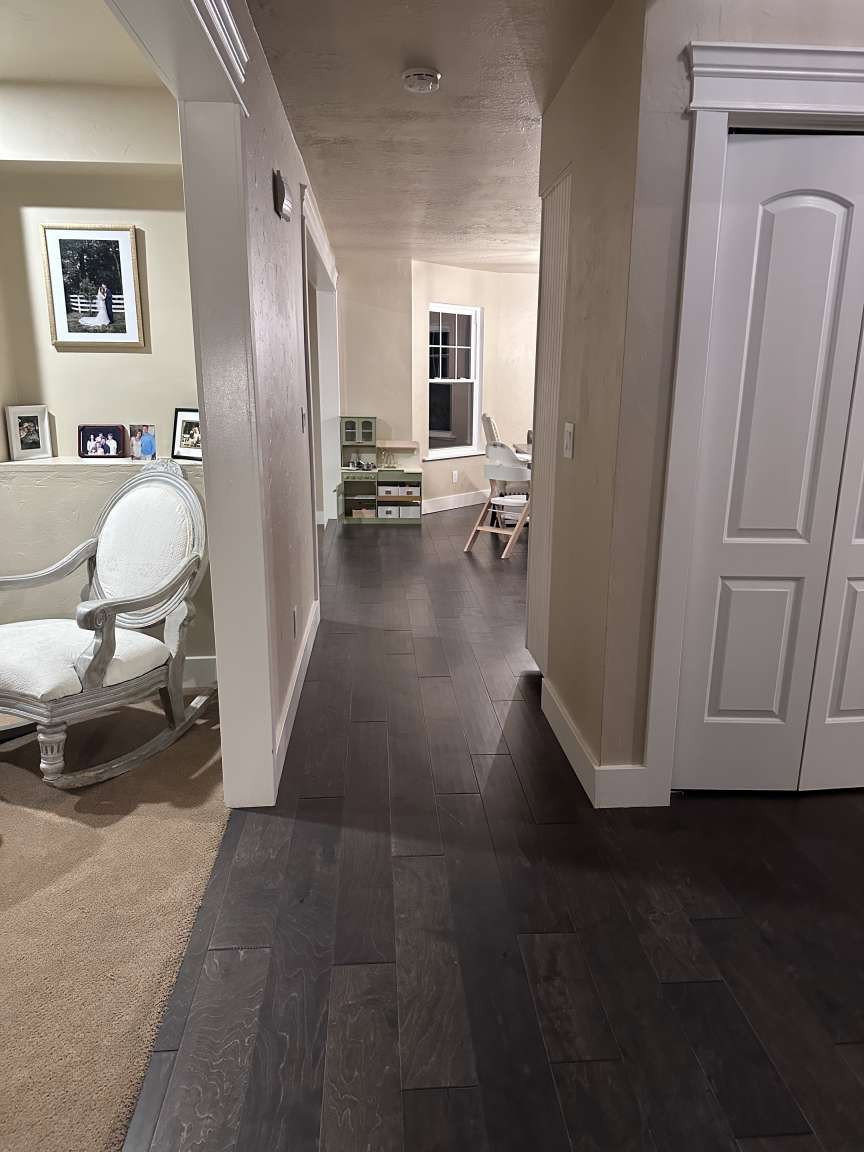 Dark wood-finish flooring extending through a hallway with light-toned walls and crisp white trim
