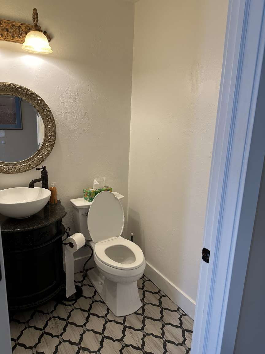 Powder room featuring a white vessel sink, black vanity with a stone-finish countertop, decorative wall mirror, and patterned floor tile