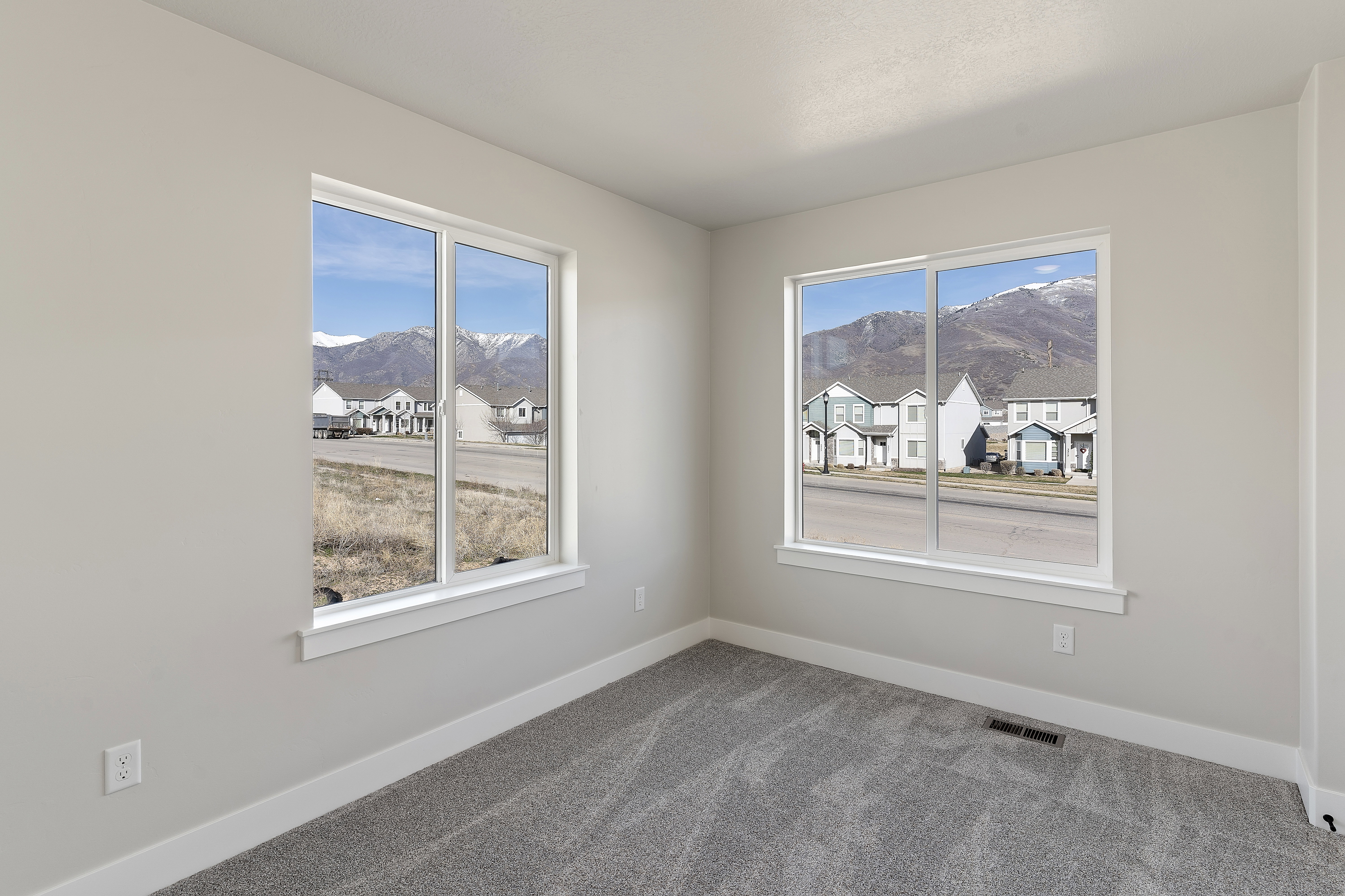 Room with two large windows, light gray walls, and gray carpet flooring