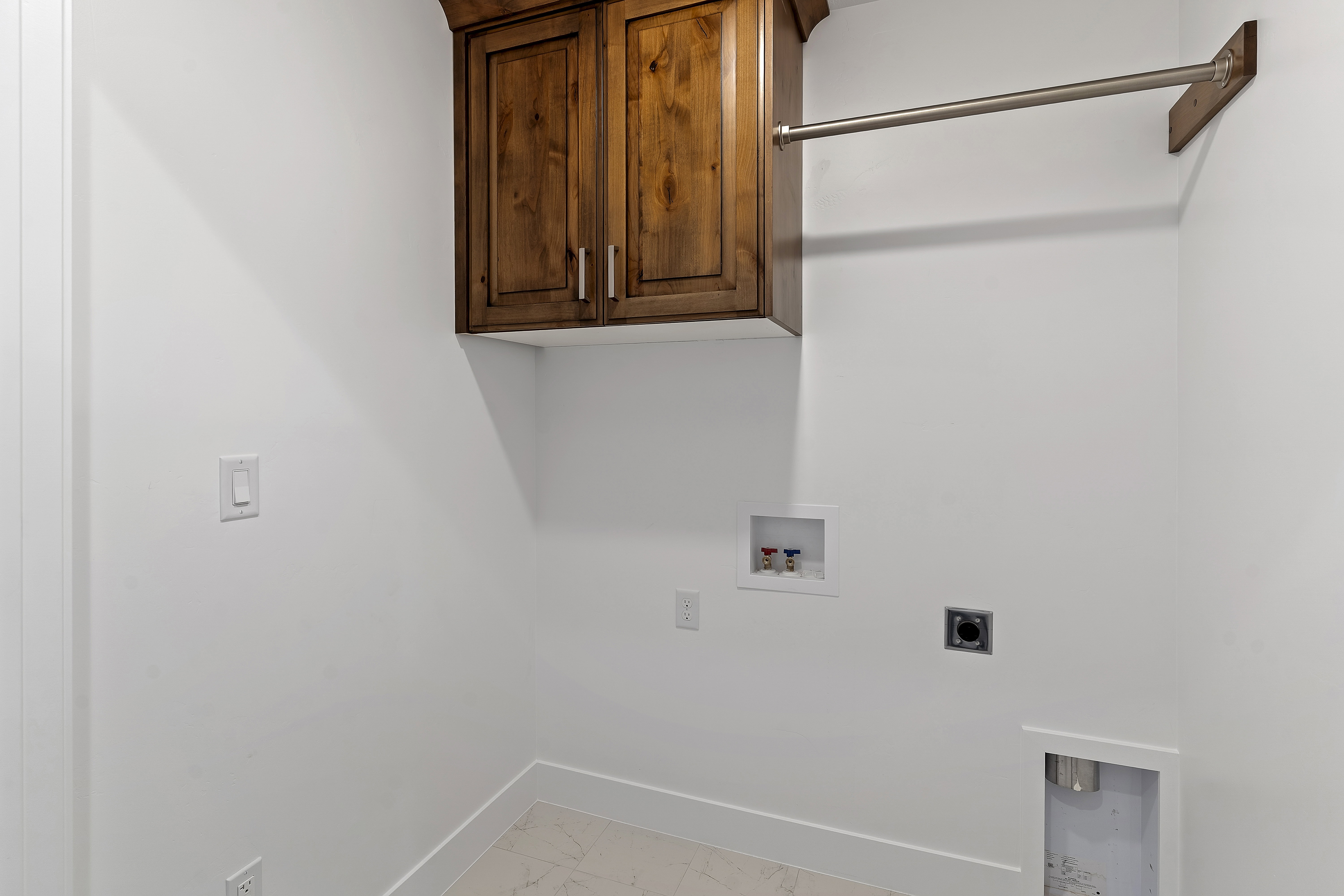 Laundry area featuring wood cabinetry, white walls, and a hanging rod