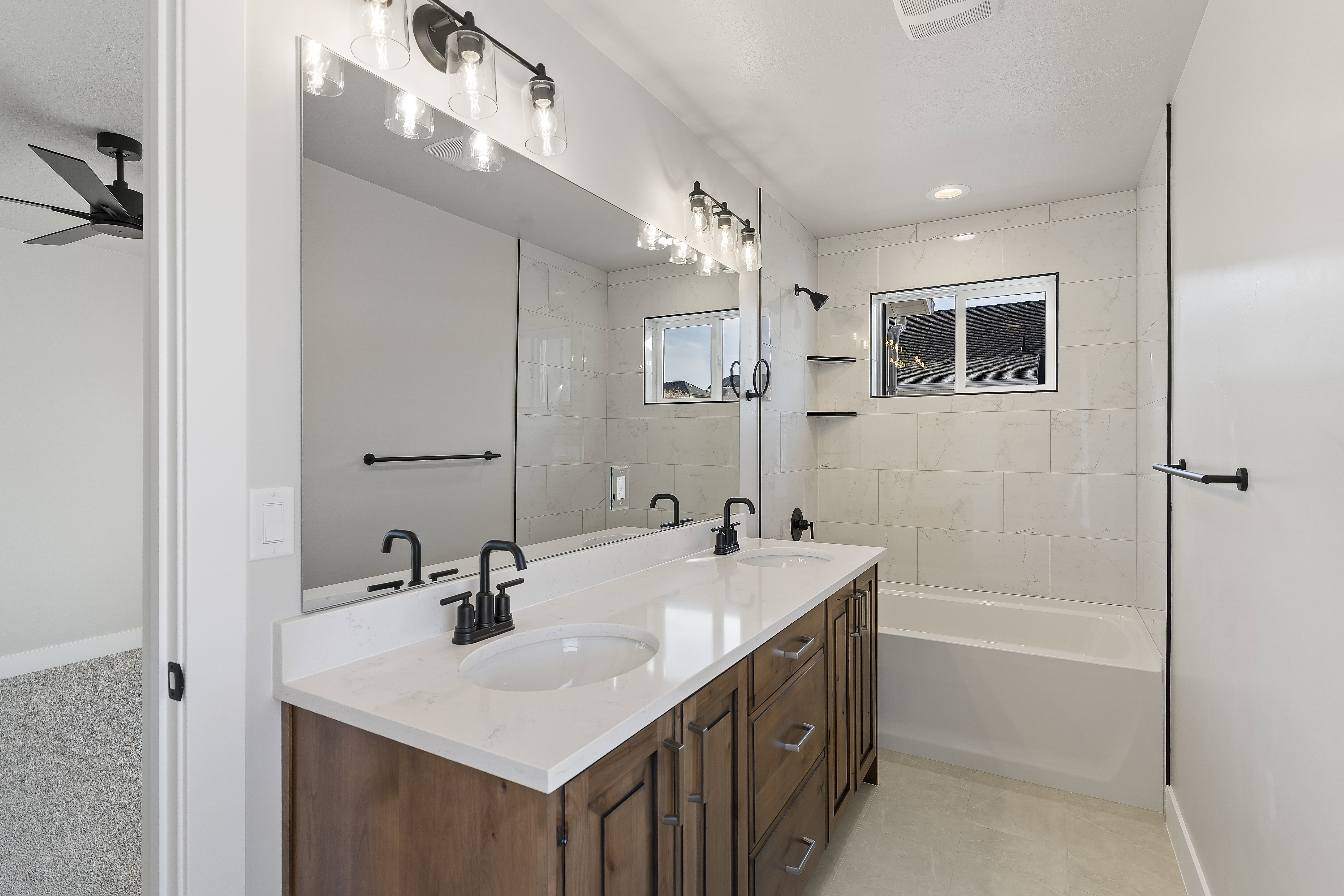 Spacious bathroom featuring a double vanity with wood-finish cabinetry and white countertops, a large mirror, dual sconce lighting, and a tiled tub and shower combination with a window