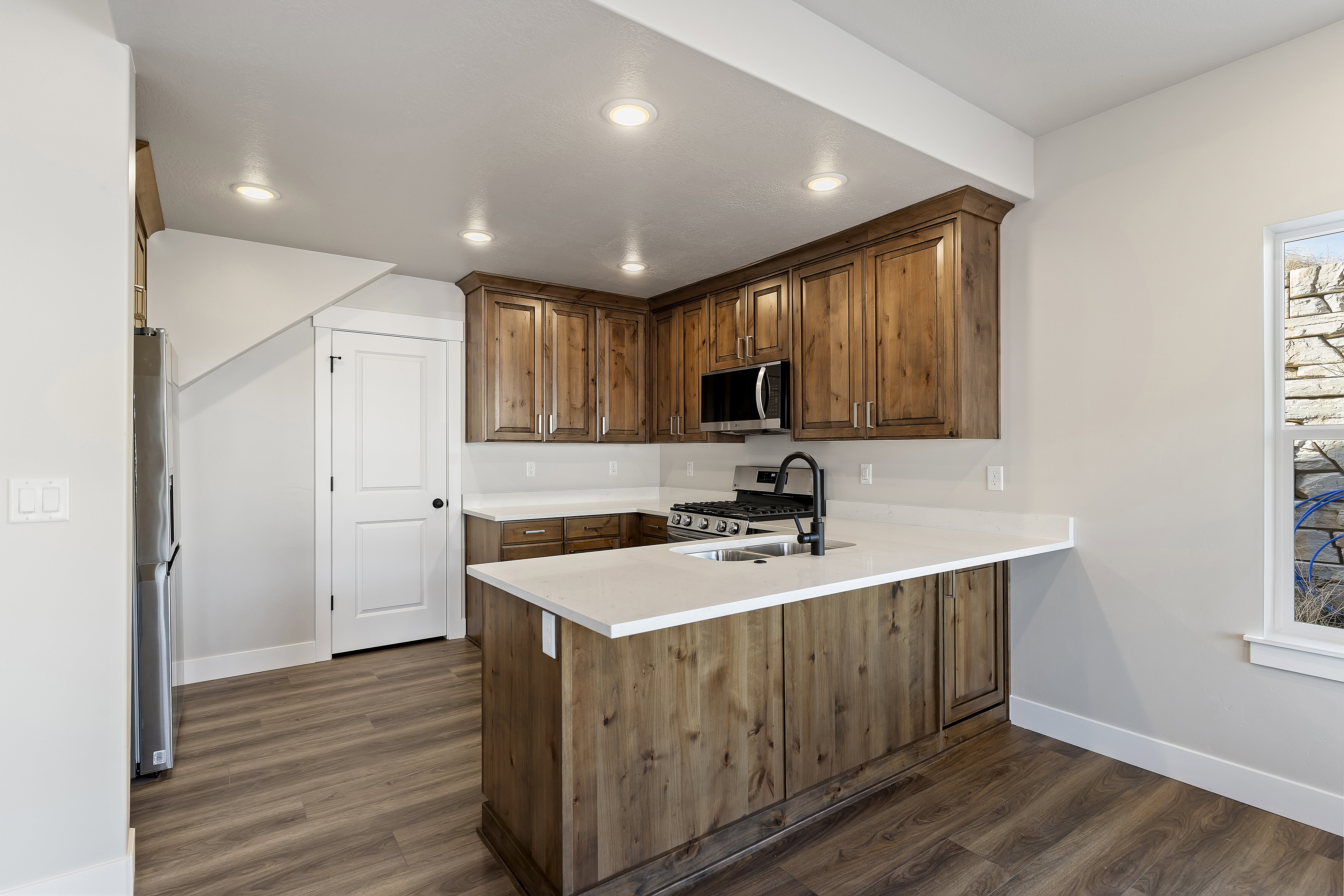 Kitchen featuring wood-finish cabinetry, stainless steel appliances, light-toned countertops, a central island with sink, and recessed lighting