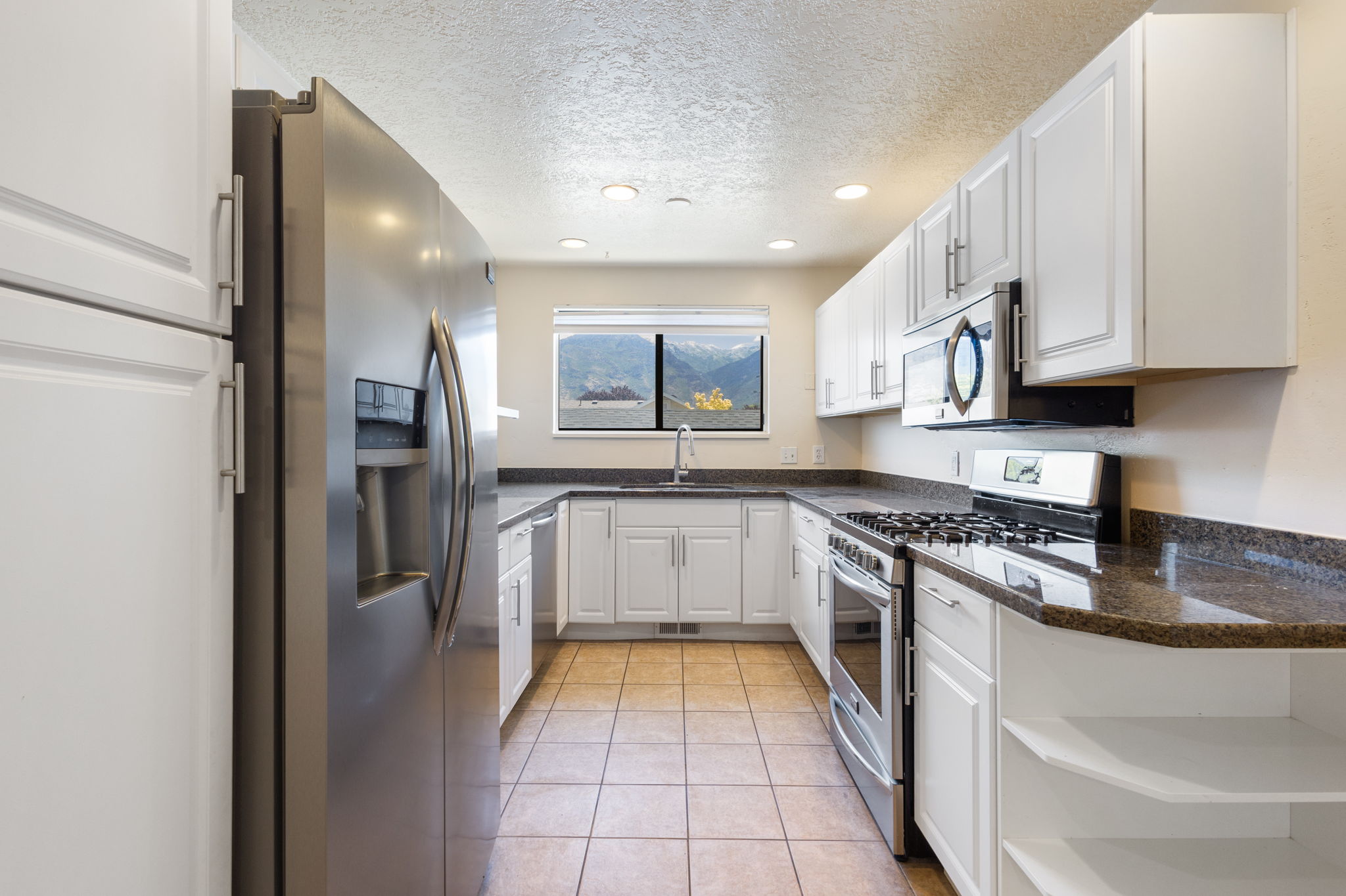 U-shaped kitchen featuring white cabinetry, dark stone countertops, stainless steel appliances, and tile flooring