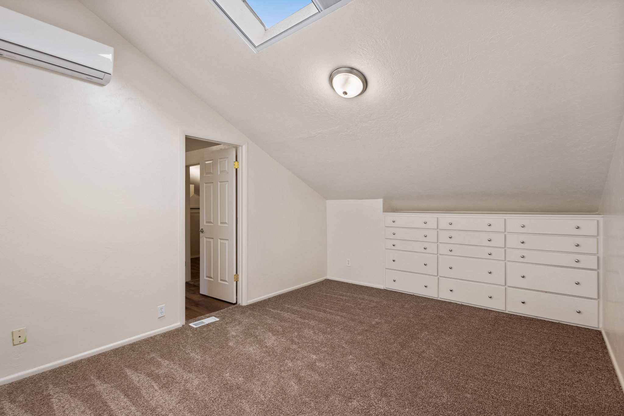 Carpeted room featuring a built-in wall of white drawers, a skylight, and a wall-mounted mini-split HVAC unit
