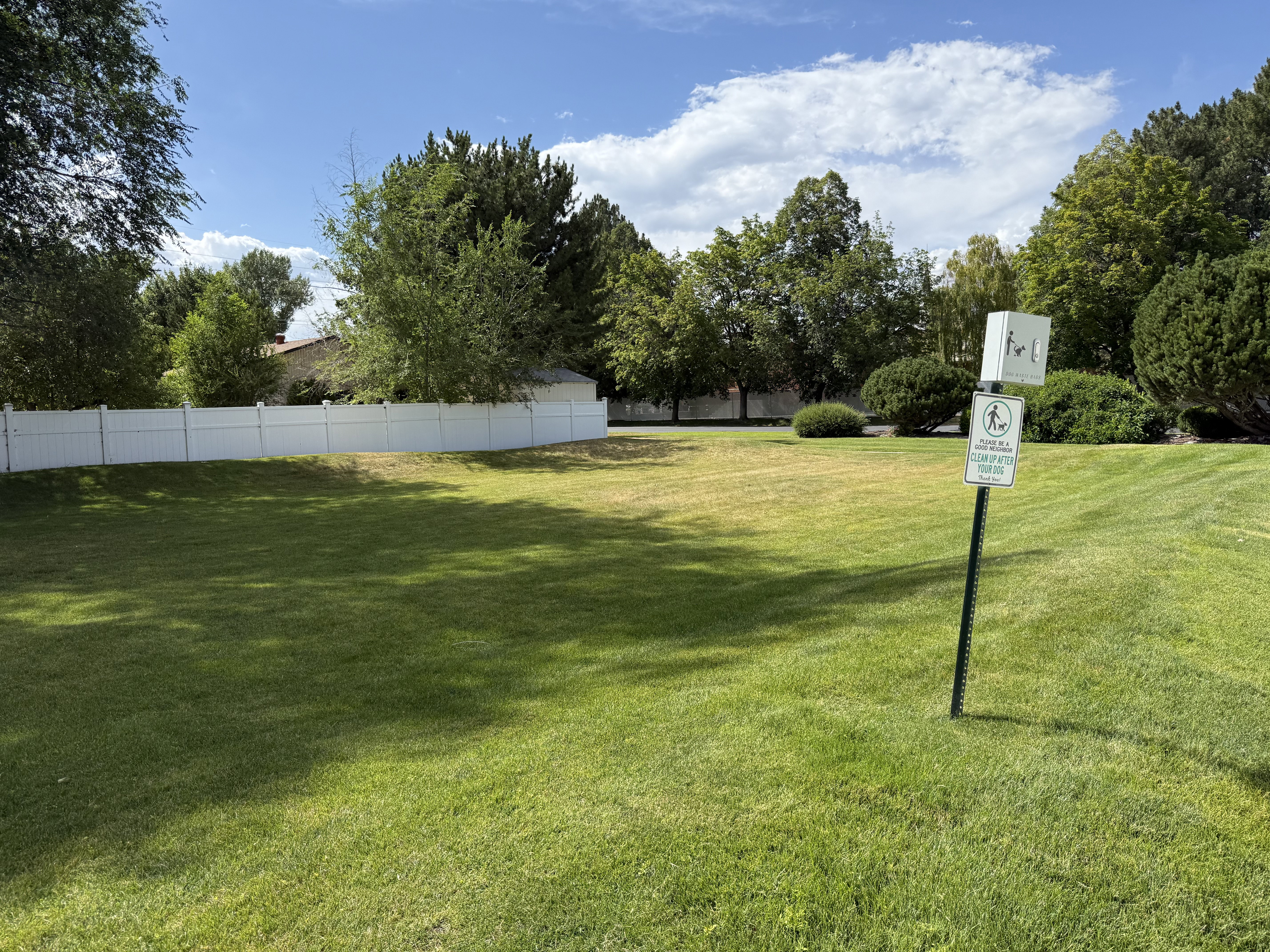 Expansive green space featuring a white privacy fence and mature perimeter trees