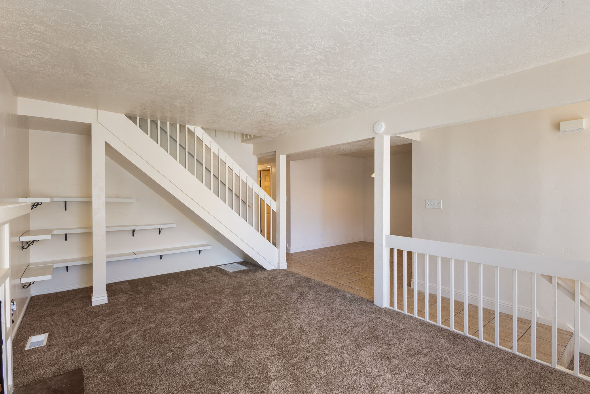 Carpeted living area featuring a white painted staircase with matching railings, built-in shelving, and neutral wall finishes