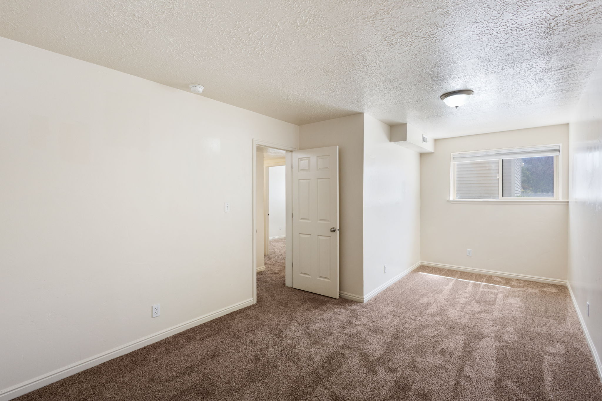 Neutral-toned room featuring a window with horizontal blinds, a ceiling-mounted light fixture, and textured ceilings