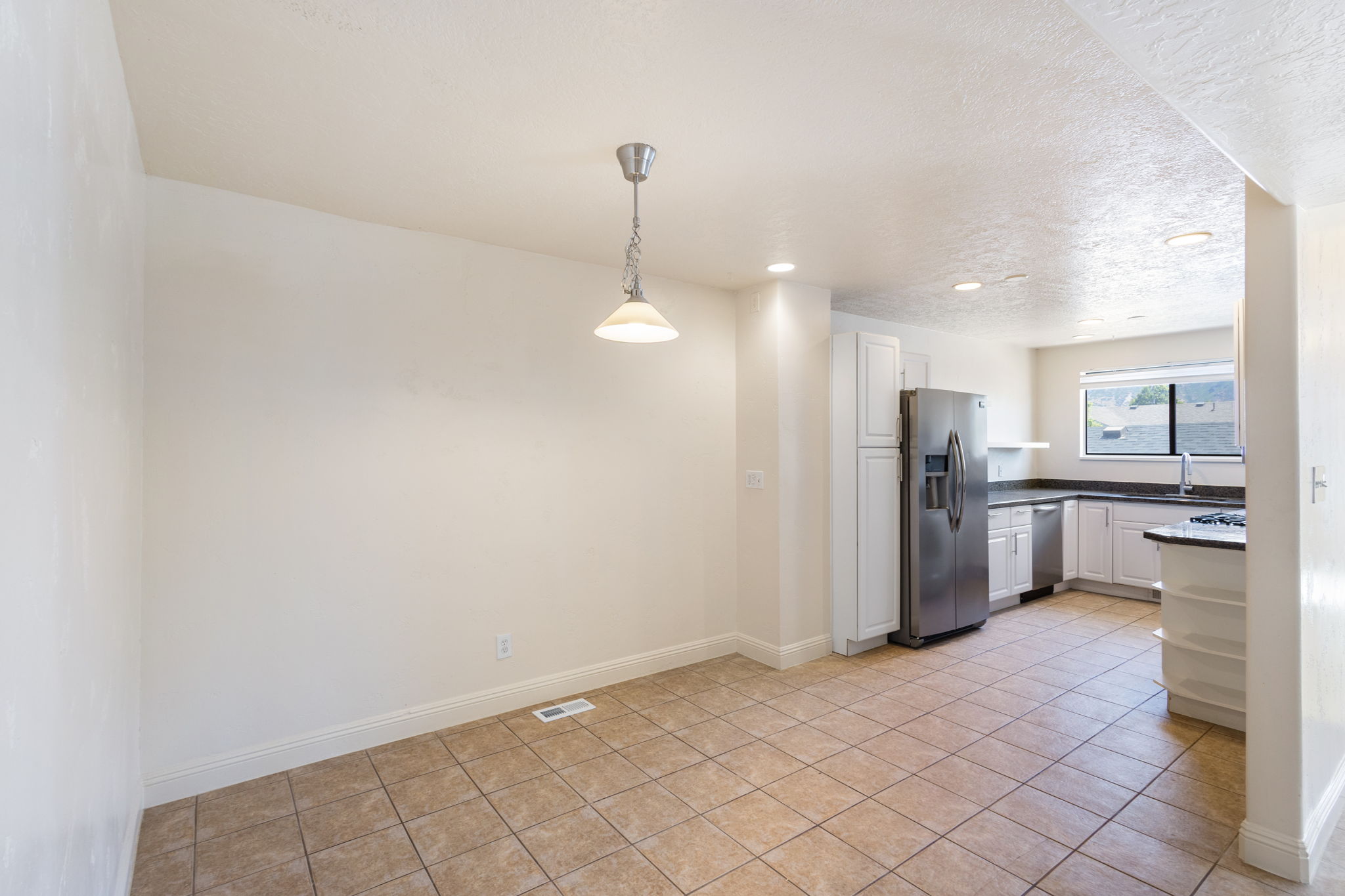Open-concept kitchen and dining area featuring tile flooring, white cabinetry, stainless steel appliances, dark countertops, and recessed lighting