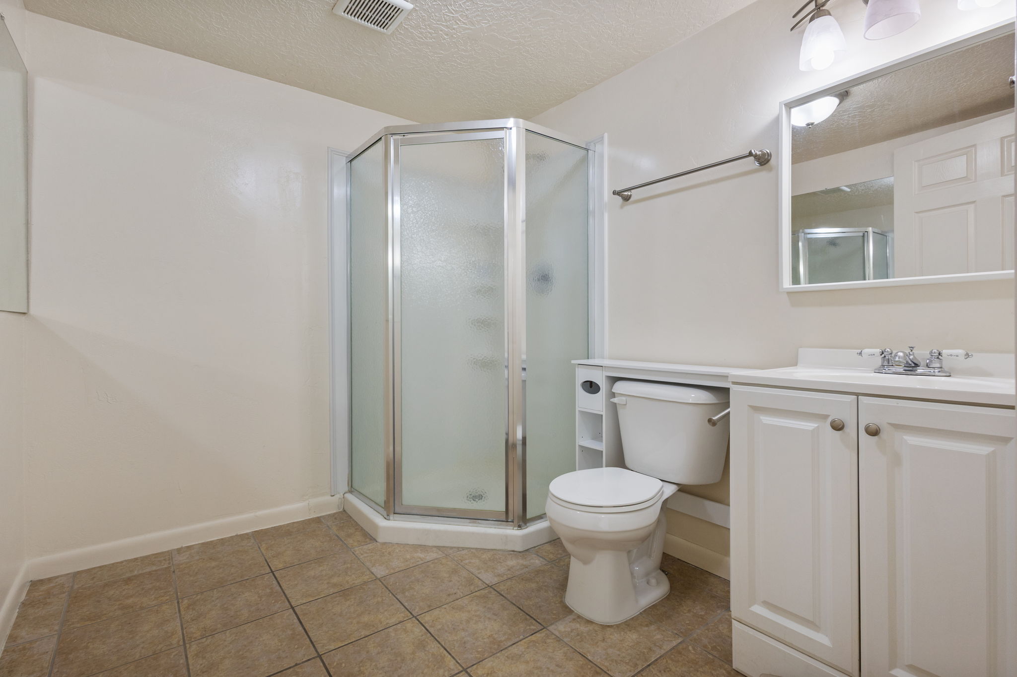 Bathroom featuring a corner shower enclosure, white vanity with integrated sink, and tile flooring