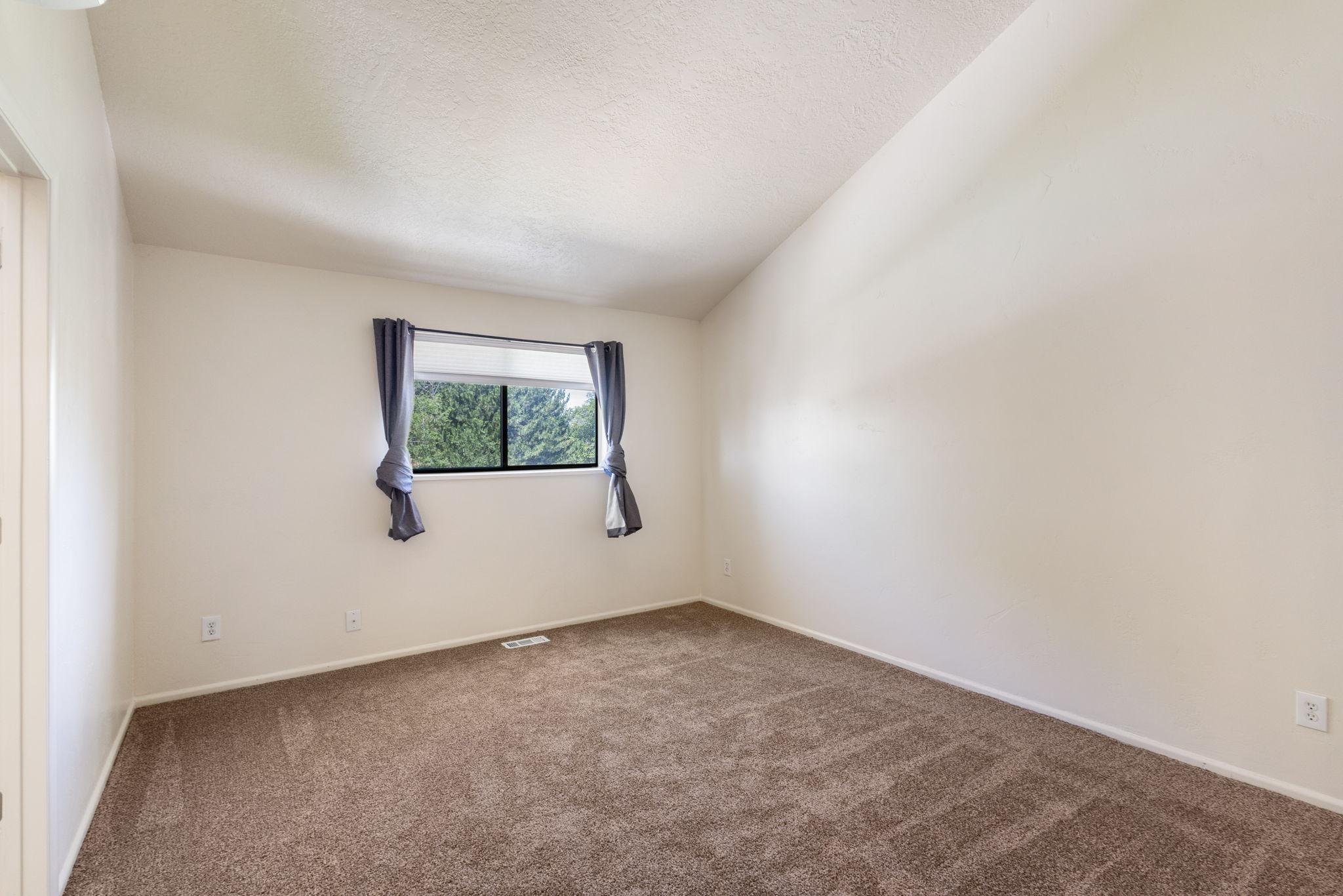 Spacious room featuring vaulted ceilings, neutral-toned walls, and brown carpeting