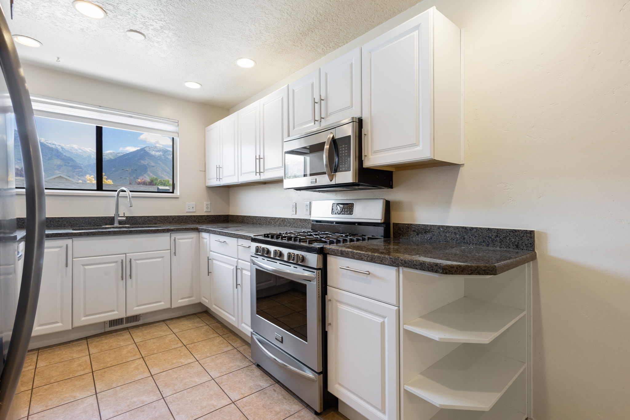 Kitchen featuring white cabinetry, dark speckled countertops, stainless steel appliances, and tile flooring