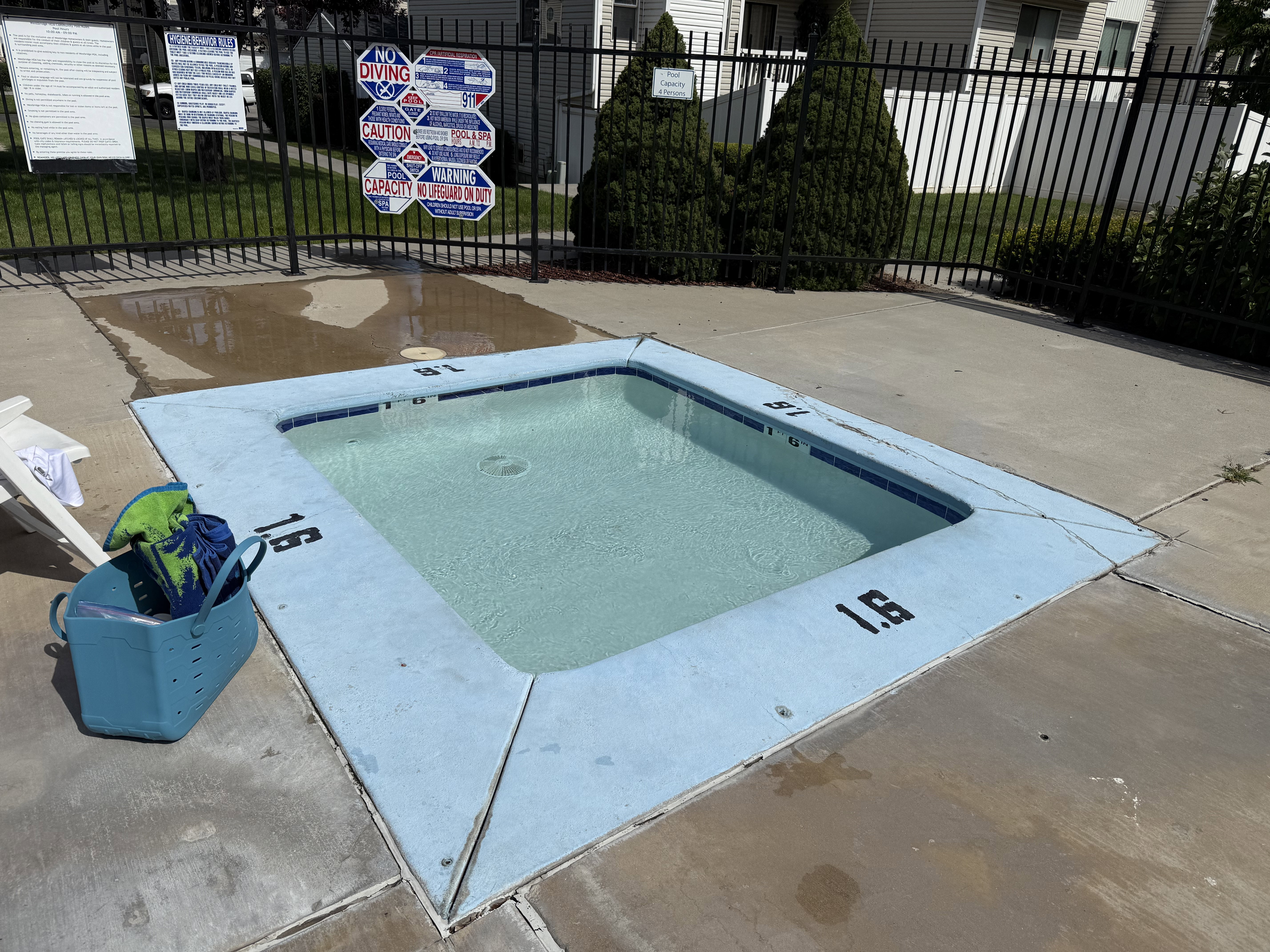 Rectangular spa with blue-tiled interior, surrounded by concrete decking and black metal fencing